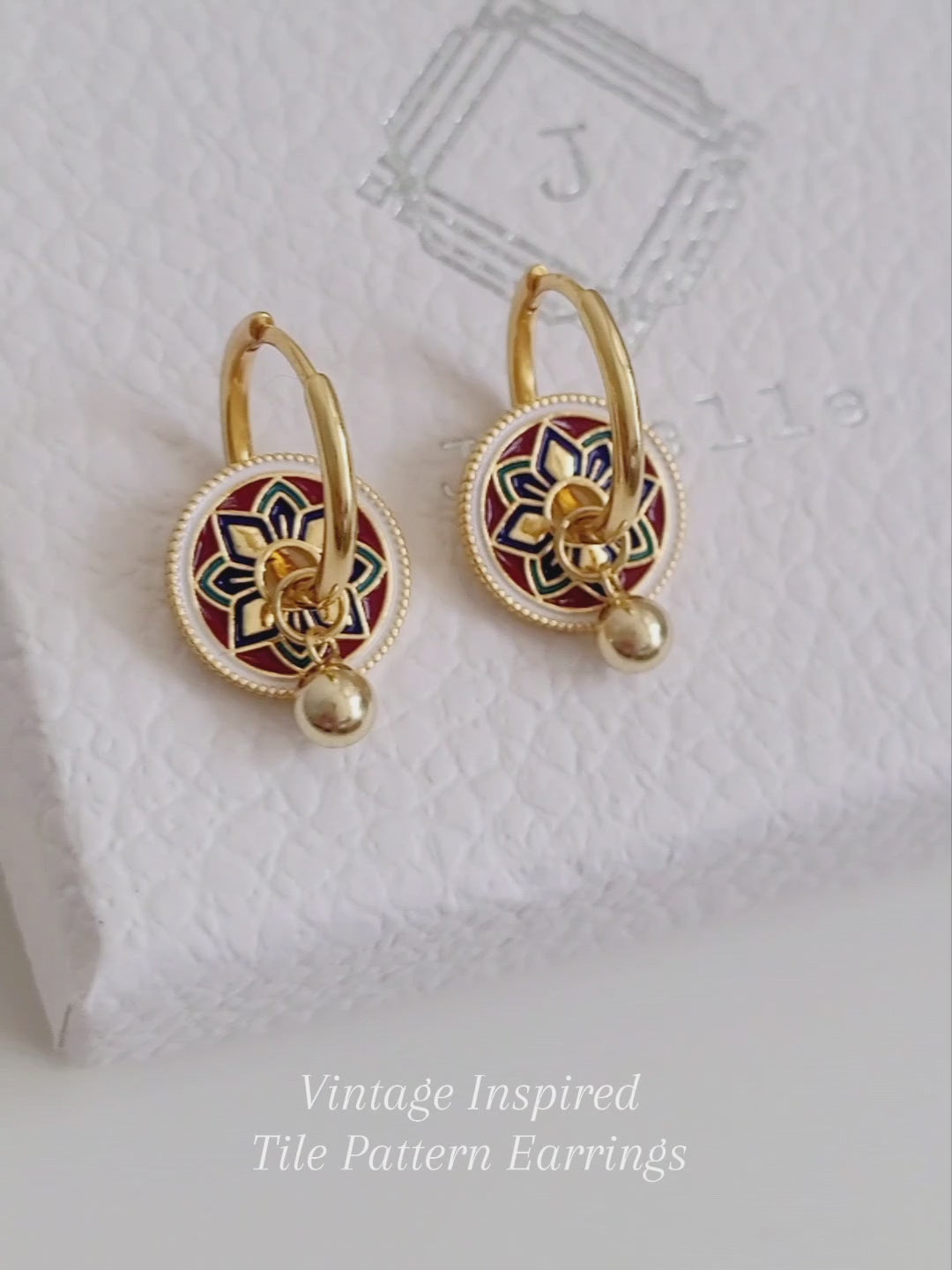 Gold hoop earrings featuring a tile pattern disc and a gold ball dangle, displayed on a white surface showcasing their elegant and unique artisan design.