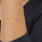 A woman elegantly showcases a gold bracelet adorned with a stunning Gold Teardrop Rutilated Quartz and Amethyst charms.