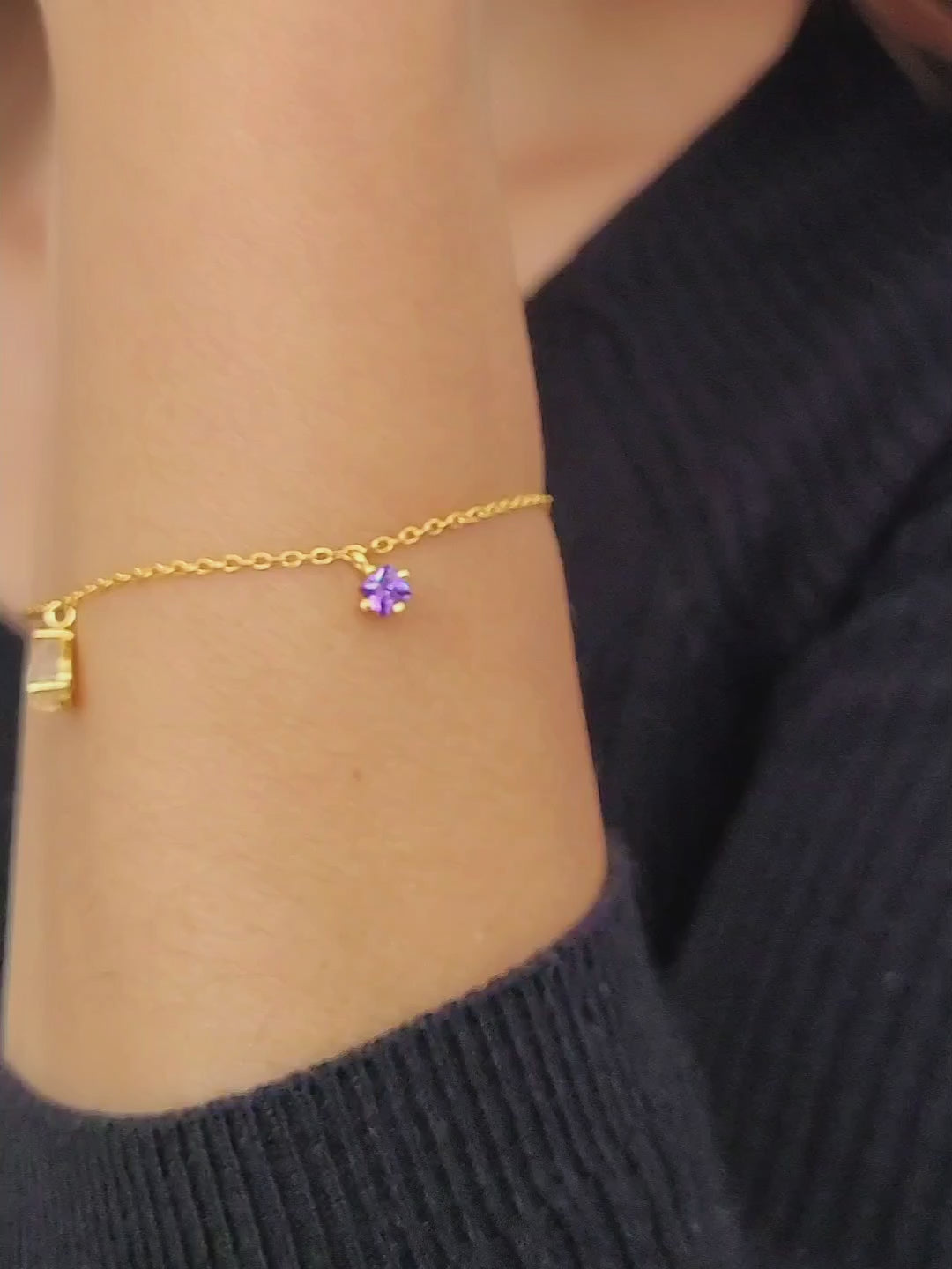 A woman elegantly showcases a gold bracelet adorned with a stunning Gold Teardrop Rutilated Quartz and Amethyst charms.