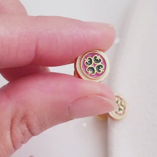 Close-up of a woman’s ear wearing a pair of Retro Gothic tile pattern enamel stud earrings in pink, dark green, and gold. The intricate design features a vintage-style pattern with a bold color combination, creating a striking and elegant look.