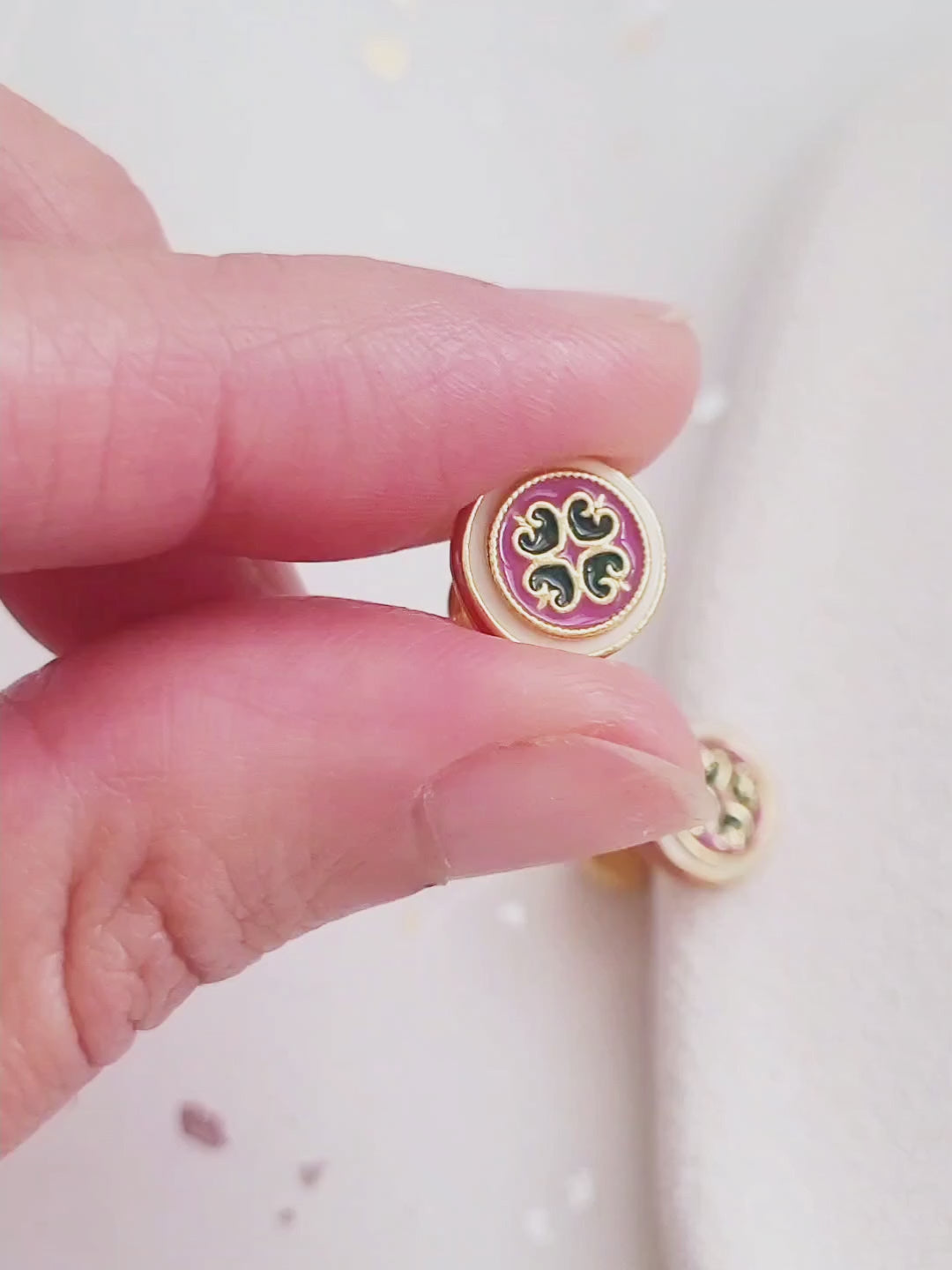 Close-up of a woman’s ear wearing a pair of Retro Gothic tile pattern enamel stud earrings in pink, dark green, and gold. The intricate design features a vintage-style pattern with a bold color combination, creating a striking and elegant look.