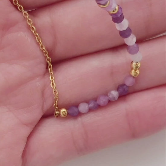 A woman wearing a dainty amethyst beaded necklace with faceted purple stones, accented by small gold beads. The necklace with a simple gold chain extending from both sides having purple hues creating a subtle yet stylish look.