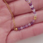 A woman wearing a dainty amethyst beaded necklace with faceted purple stones, accented by small gold beads. The necklace with a simple gold chain extending from both sides having purple hues creating a subtle yet stylish look.