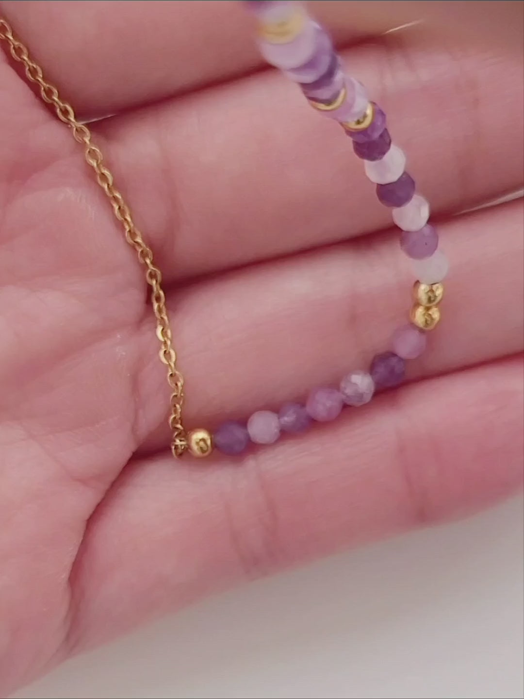 A woman wearing a dainty amethyst beaded necklace with faceted purple stones, accented by small gold beads. The necklace with a simple gold chain extending from both sides having purple hues creating a subtle yet stylish look.