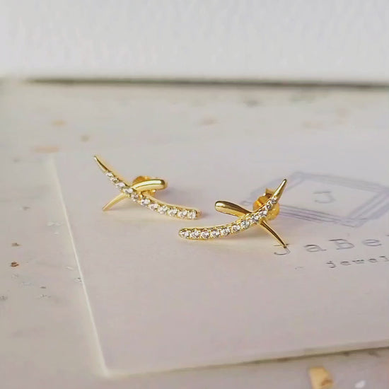 A pair of gold cross stud earrings with cubic zirconia stones displayed on an elegant white surface