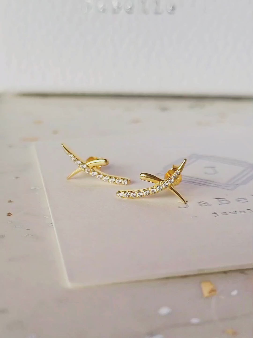 A pair of gold cross stud earrings with cubic zirconia stones displayed on an elegant white surface