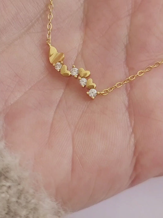 Close-up of a dainty gold necklace with heart charms and sparkling diamond accents, perfect for weddings, bridal showers, and Valentine’s Day.