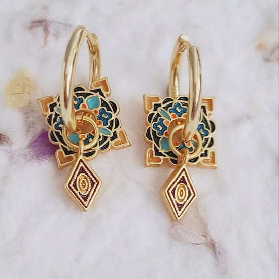 Artistic gold hoop earrings adorned with vibrant enamel tile motifs and small diamond-shaped pendants, perfect for a unique statement look.