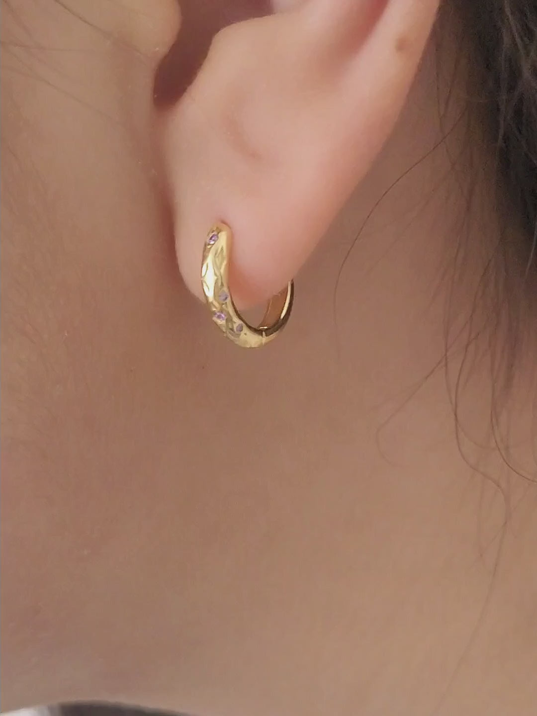 Close up of a woman wearing 18k gold plated sterling silver huggie hoop earrings with purple crystals, featuring a cosmic star inspired design.