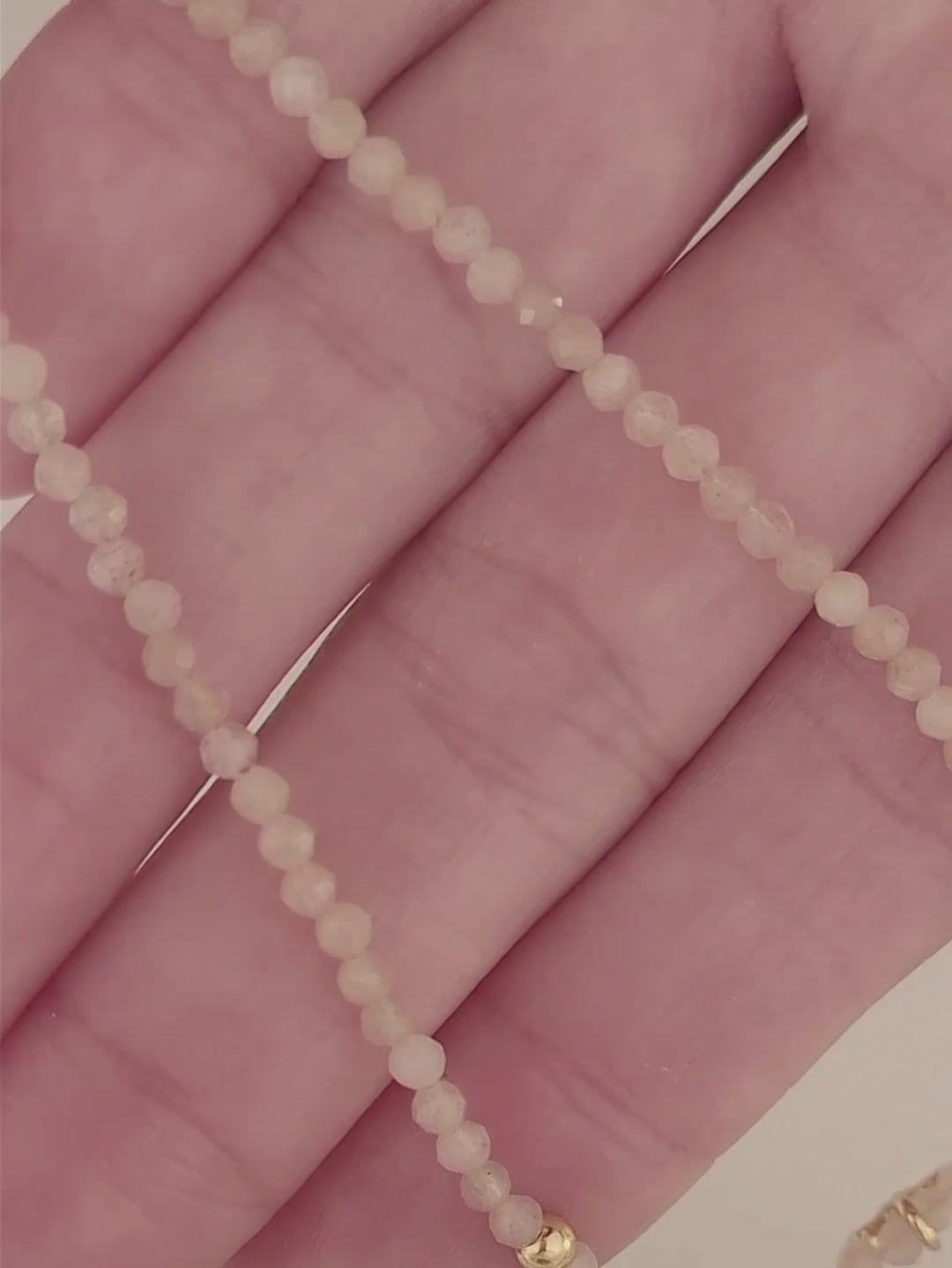 Close-up of a woman wearing an elegant sunstone beaded necklace with a mini clover pendant in gold.