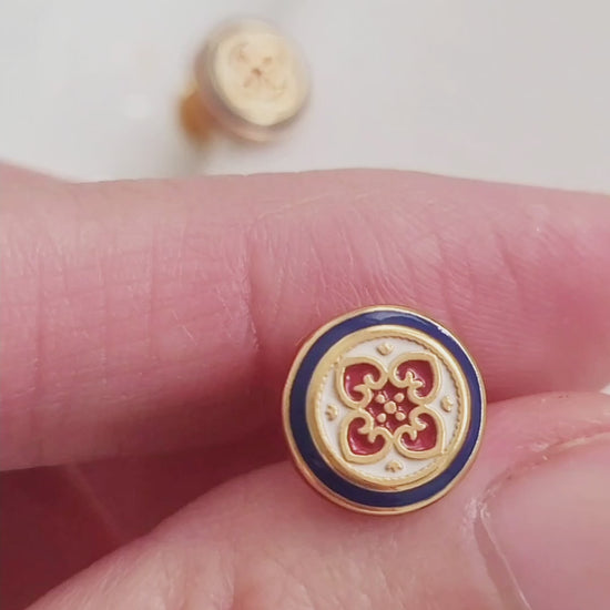 Close-up of a woman's ear wearing a pair of Retro Gothic tile pattern enamel stud earrings in red, blue, and gold. The intricate design features a vintage-style pattern with a bold color combination, creating a striking and elegant look."