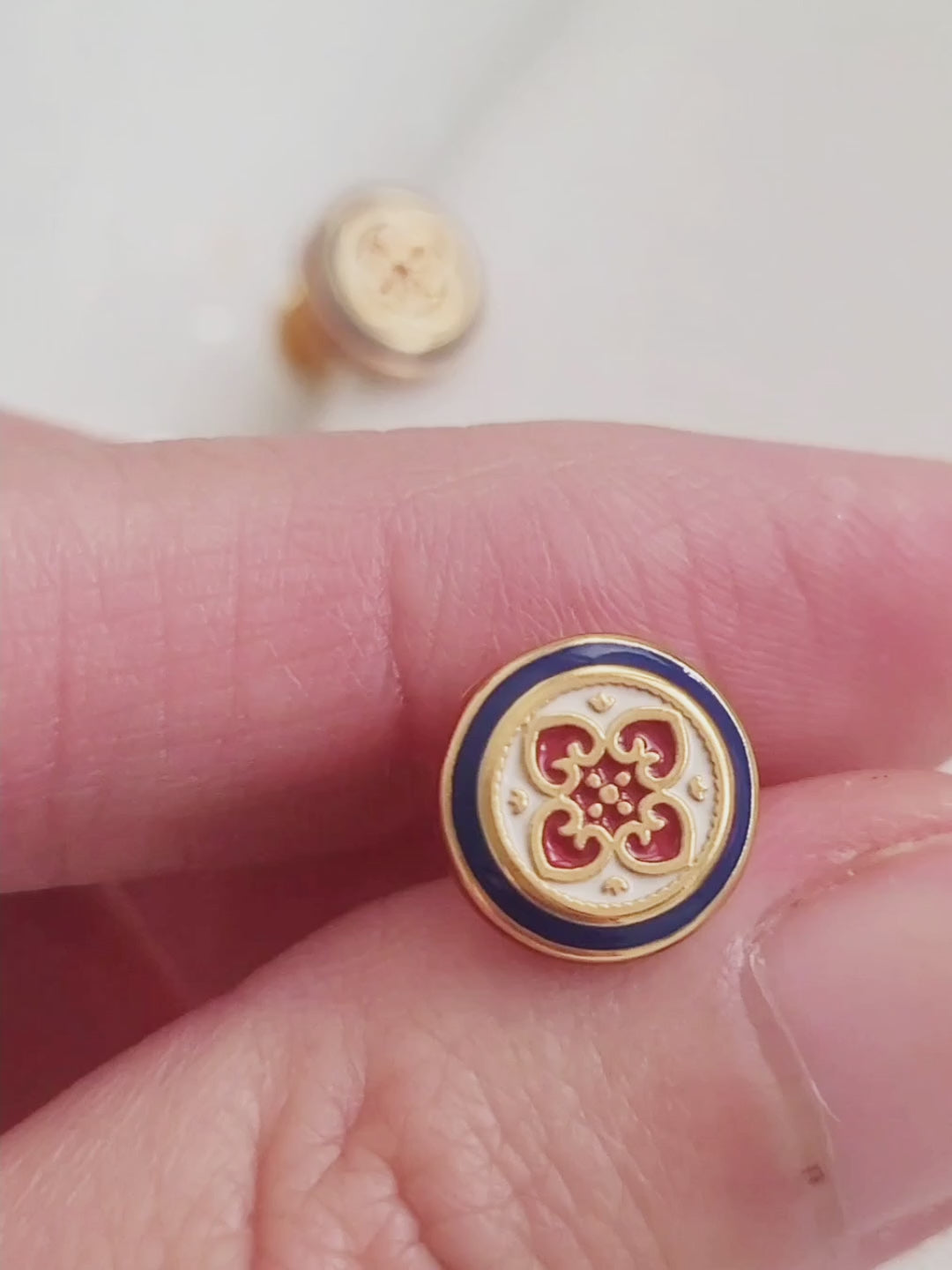 Close-up of a woman's ear wearing a pair of Retro Gothic tile pattern enamel stud earrings in red, blue, and gold. The intricate design features a vintage-style pattern with a bold color combination, creating a striking and elegant look."