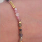 Close-up of a woman's waist wearing a dainty rainbow gemstone bracelet featuring faceted aventurine, jasper, and rose quartz beads, accented with gold vermeil heart charm at the center. The bracelet has a gold clasp and adjustable chain.