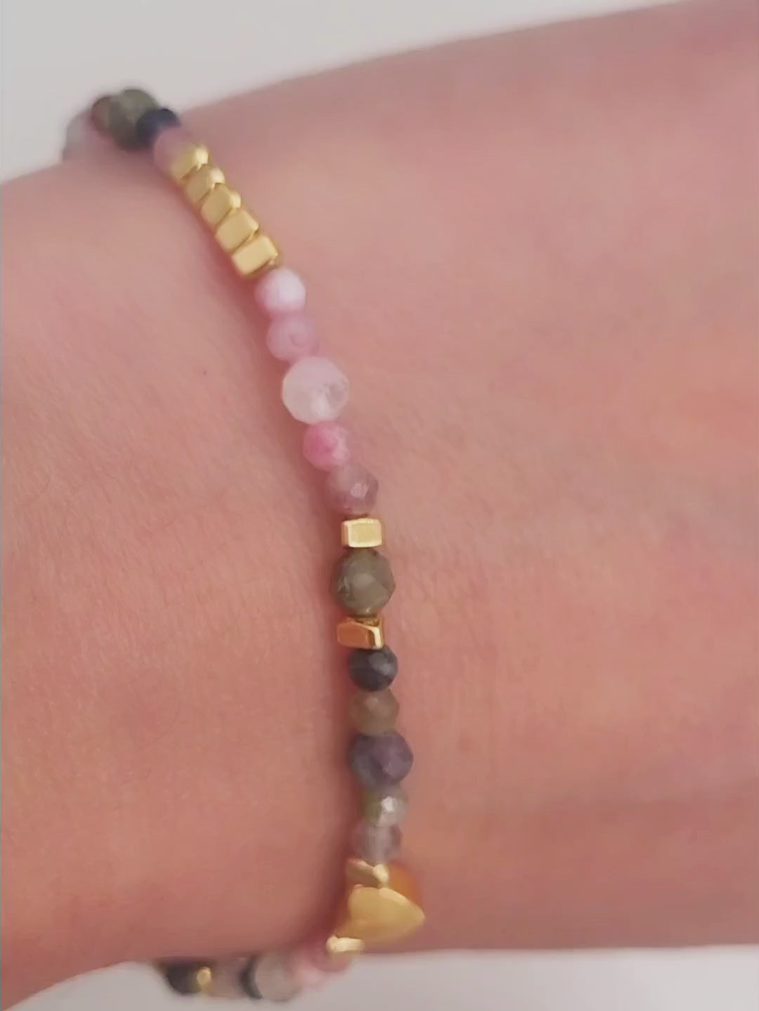 Close-up of a woman's waist wearing a dainty rainbow gemstone bracelet featuring faceted aventurine, jasper, and rose quartz beads, accented with gold vermeil heart charm at the center. The bracelet has a gold clasp and adjustable chain.