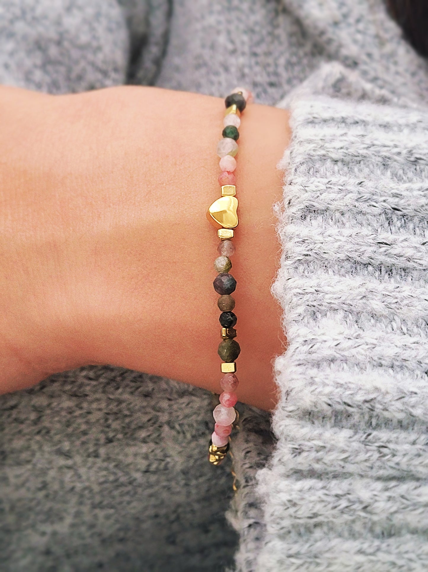 Close-up of a woman's waist wearing a dainty rainbow gemstone bracelet featuring faceted aventurine, jasper, and rose quartz beads, accented with gold vermeil heart charm at the center. The bracelet has a gold clasp and adjustable chain.