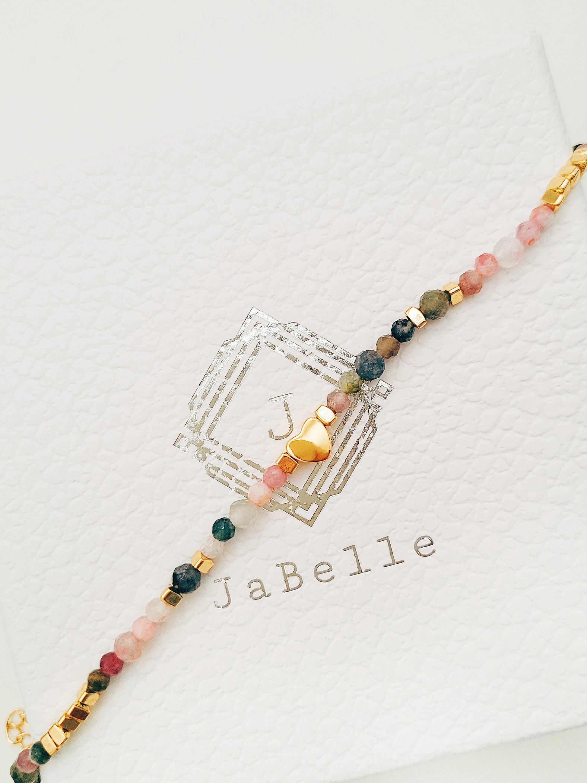 A delicate rainbow gemstone bracelet featuring faceted aventurine, jasper, and rose quartz beads, accented with gold vermeil heart charm at the center. The bracelet has a gold clasp and adjustable chain.