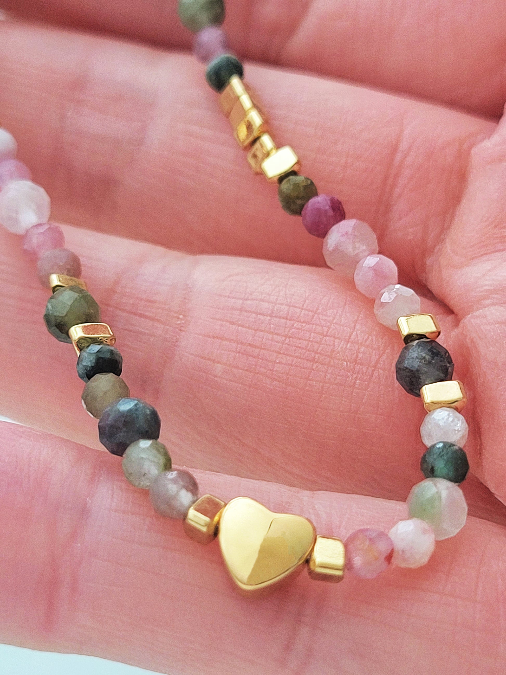 A delicate rainbow gemstone bracelet featuring faceted aventurine, jasper, and rose quartz beads, accented with gold vermeil heart charm at the center. The bracelet has a gold clasp and adjustable chain.