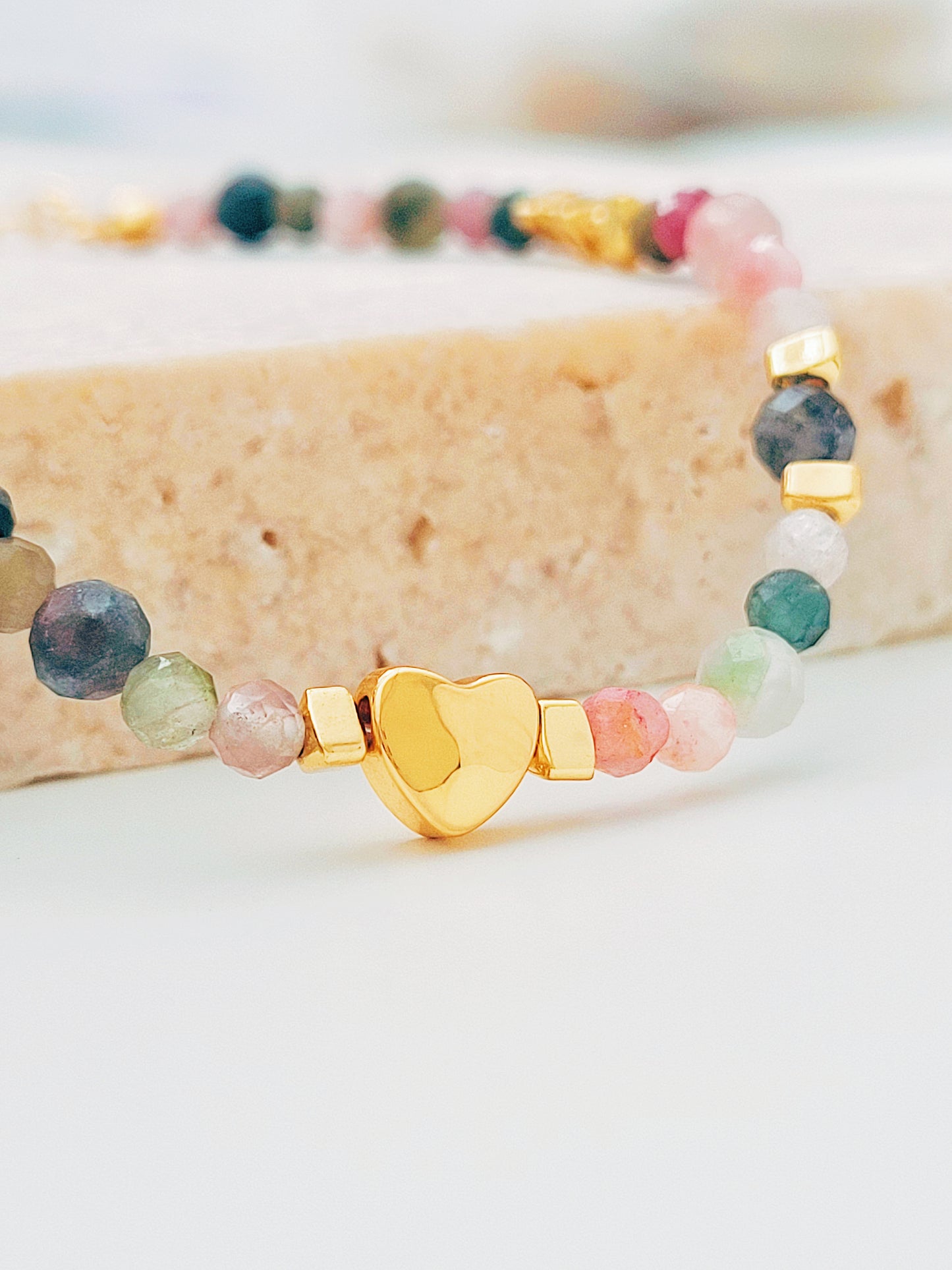 Close-up of a delicate rainbow gemstone bracelet featuring faceted aventurine, jasper, and rose quartz beads, accented with a gold vermeil heart charm at the center. The bracelet has a gold clasp and adjustable chain.