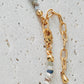 Close-up of a delicate multi-gemstone necklace featuring small, irregular-shaped beads in various shades of blue, gold, and brown. The necklace has a subtle, earthy color palette with gold accents and natural stones, creating a minimalistic yet bohemian aesthetic. 