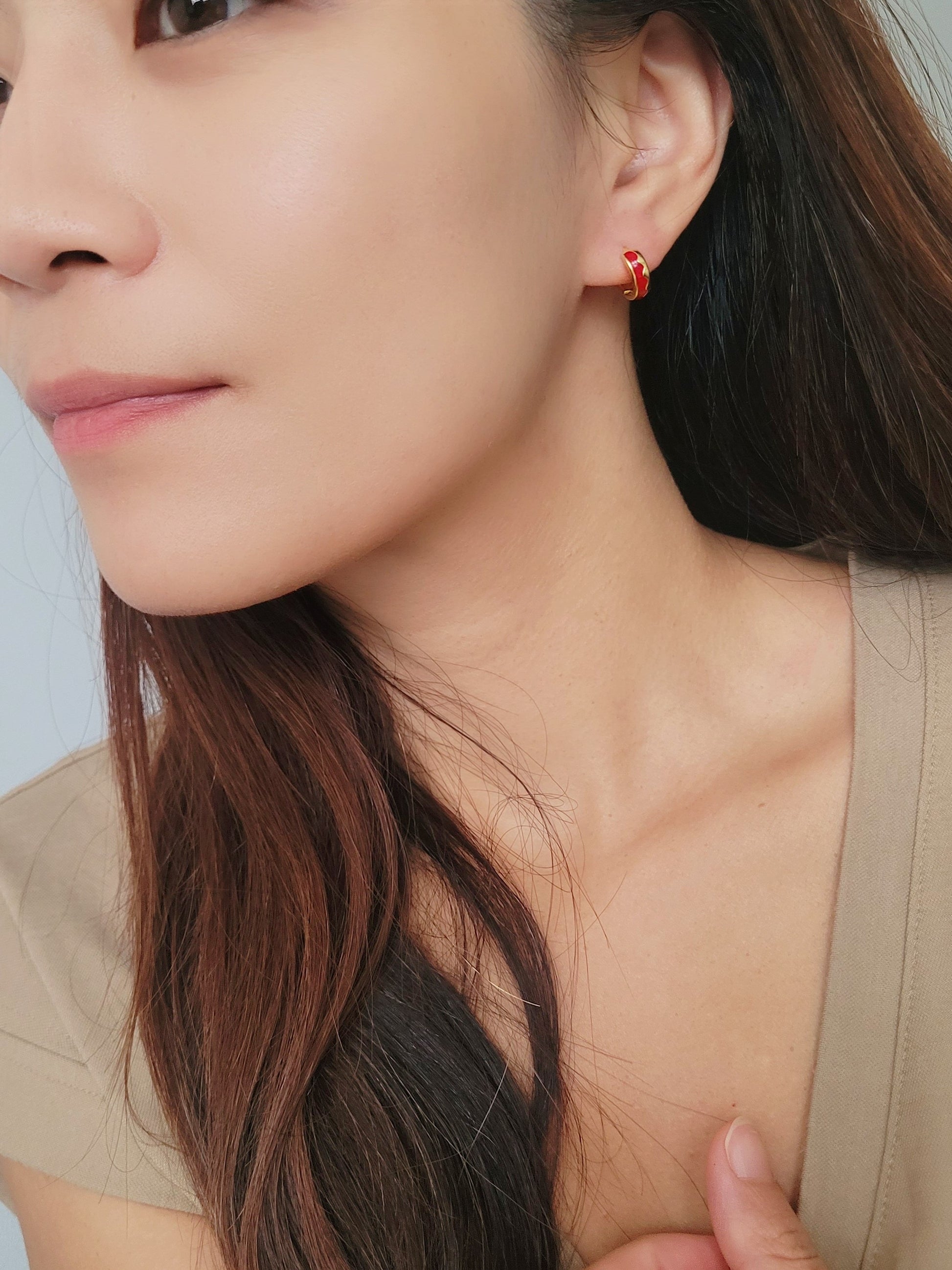 A woman showcasing her trendy red enamel hoop earrings. 