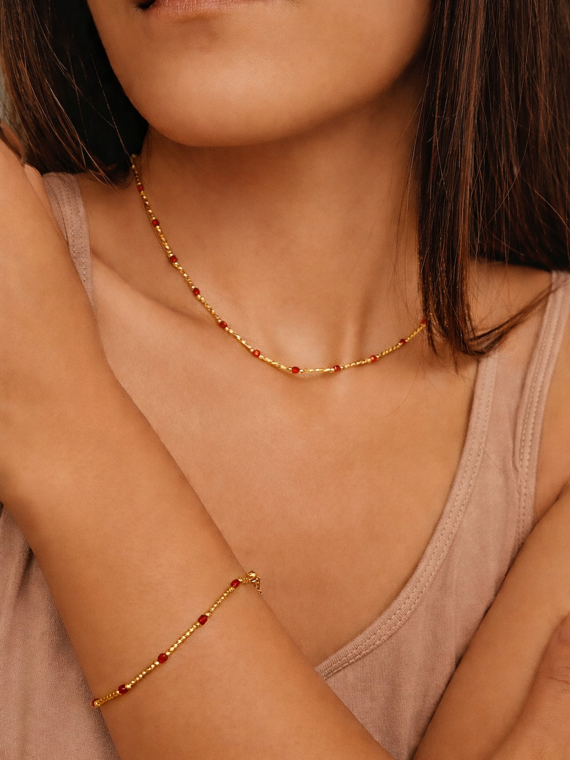 Close-up of a woman wearing a gold necklace and bracelet with red onyx stones.