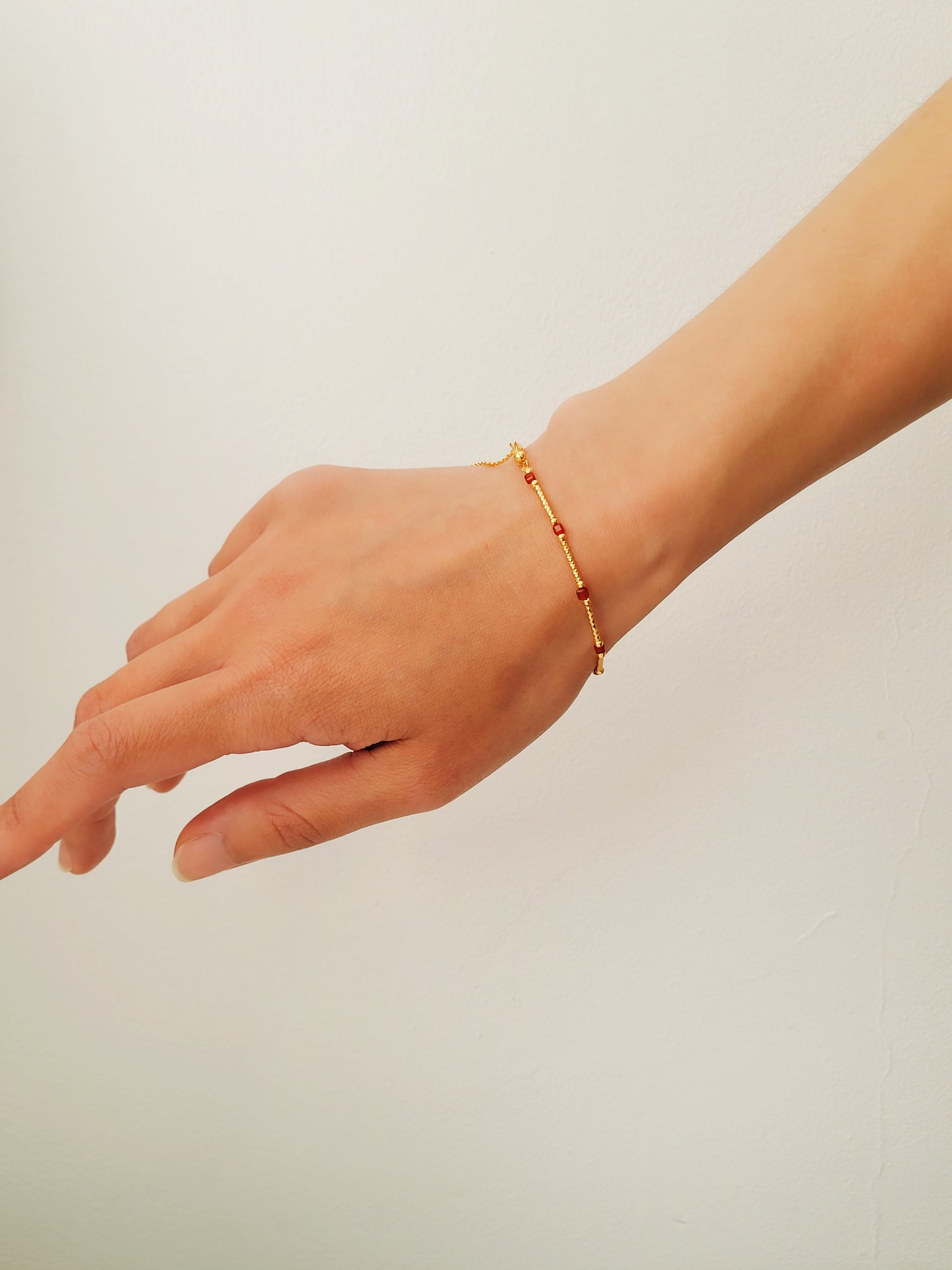 A gold bracelet with red onyx gemstone worn on a woman's wrist.