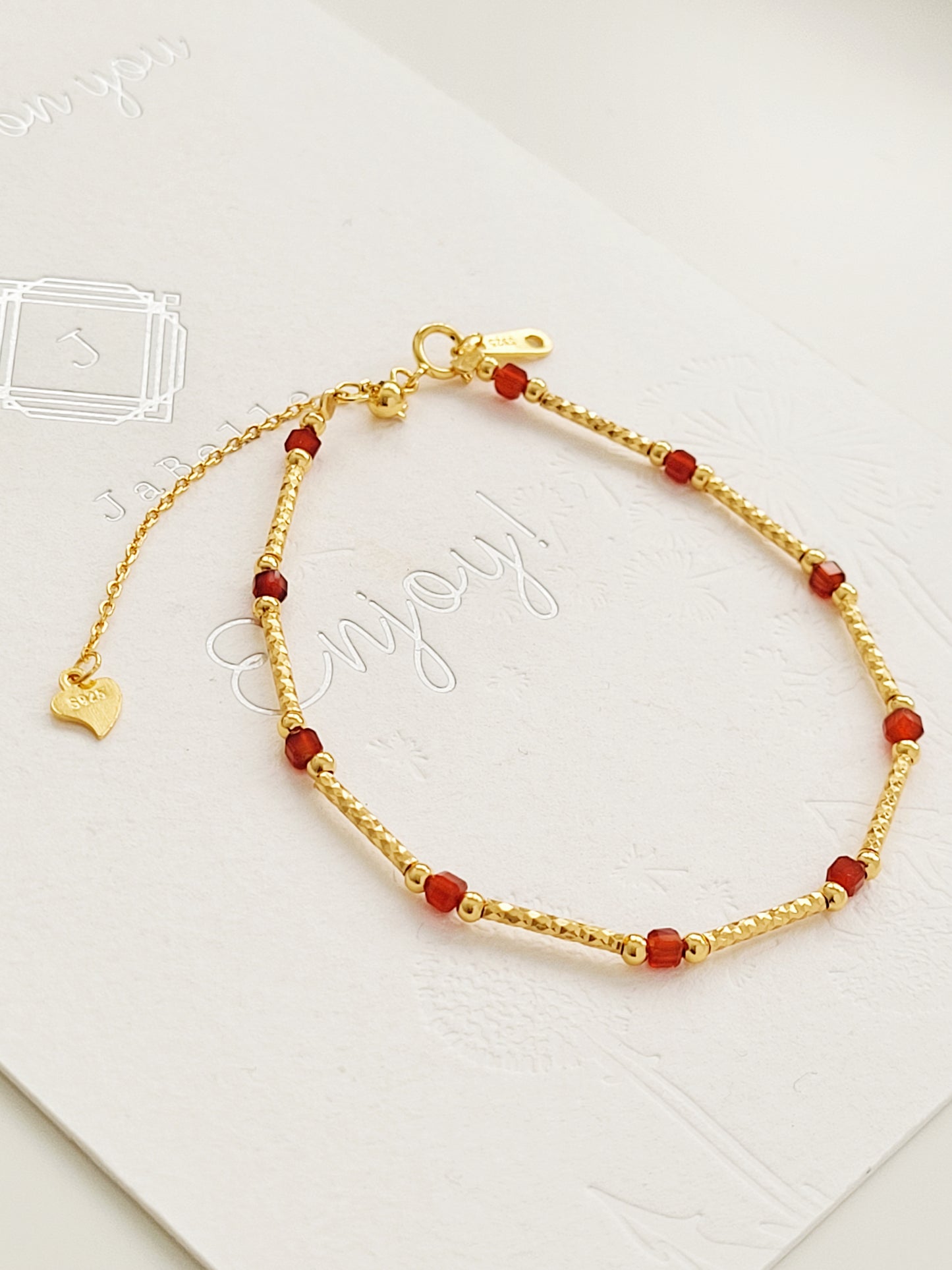 A dainty gold bracelet with red onyx displayed on JaBelle Jewellery card.
