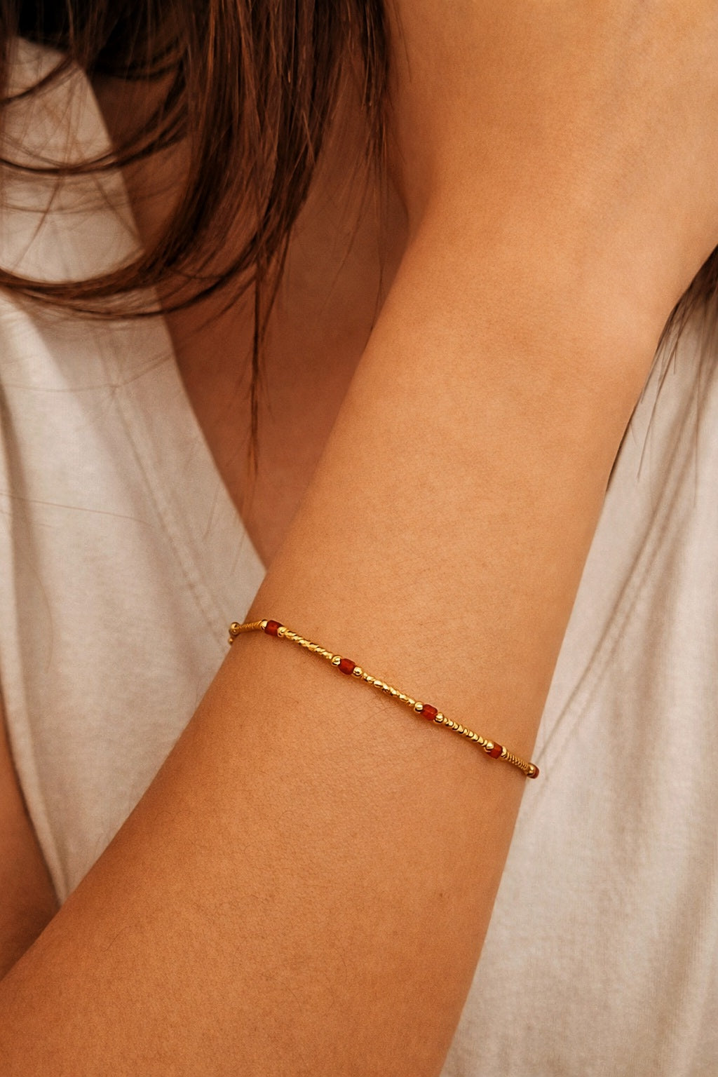 Gold bracelet with red onyx gemstone on a woman's wrist, she dressed in casual outfit.
