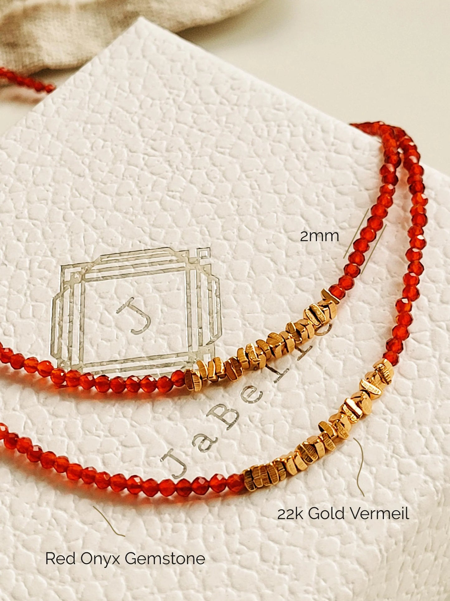 Two beaded necklaces featuring red onyx gemstone and 22k gold vermeil nuggets displayed on a textured white surface.