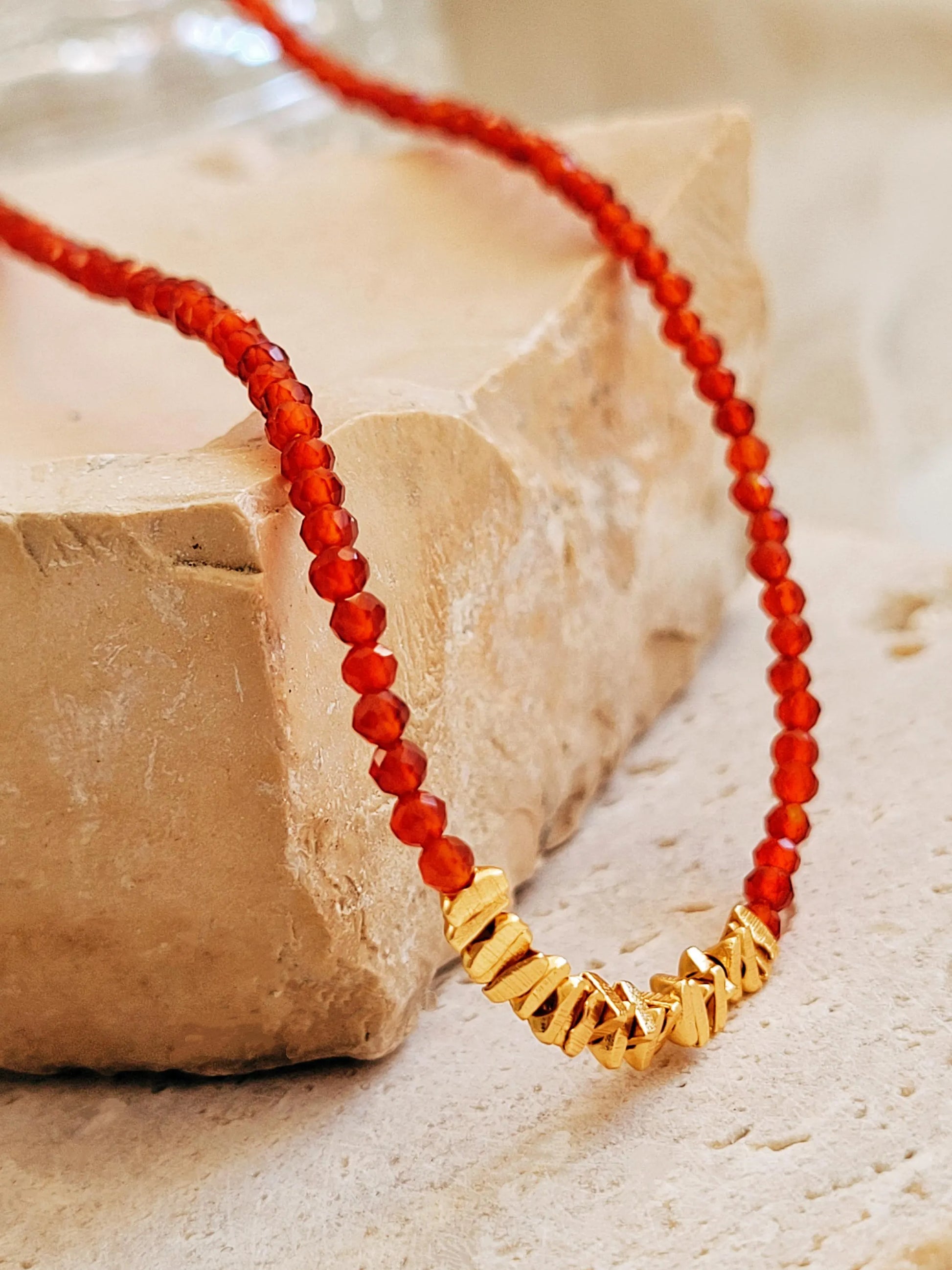 Close up of a red onyx gold vermeil choker necklace on an aesthetic beige color stone.