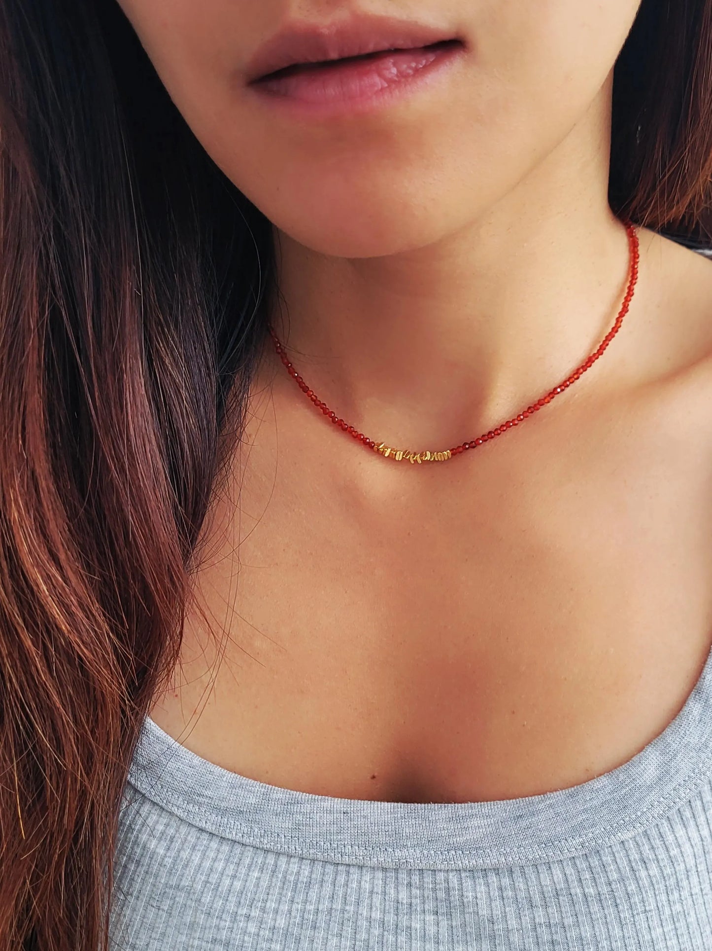 Close-up of a person wearing a red beaded necklace with a gold clasp.