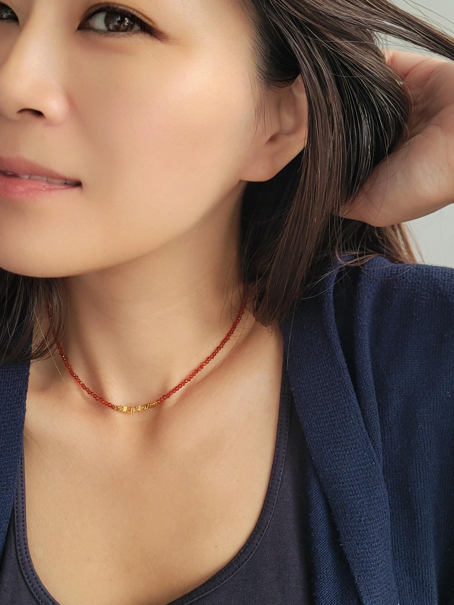 Close-up of a woman wearing a red onyx beaded choker necklace with a neutral background