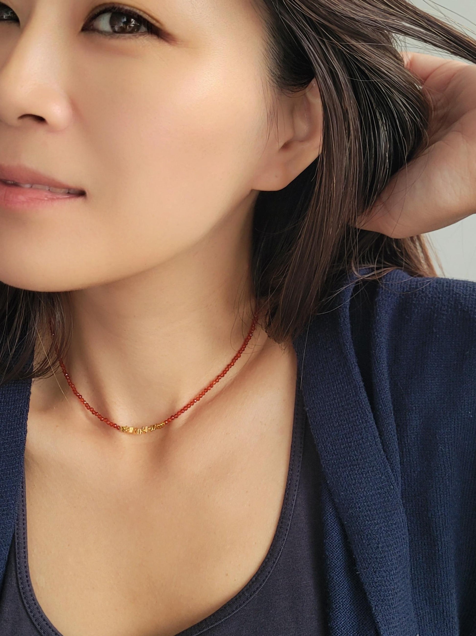 Close-up of a woman wearing a red onyx beaded choker necklace with a neutral background