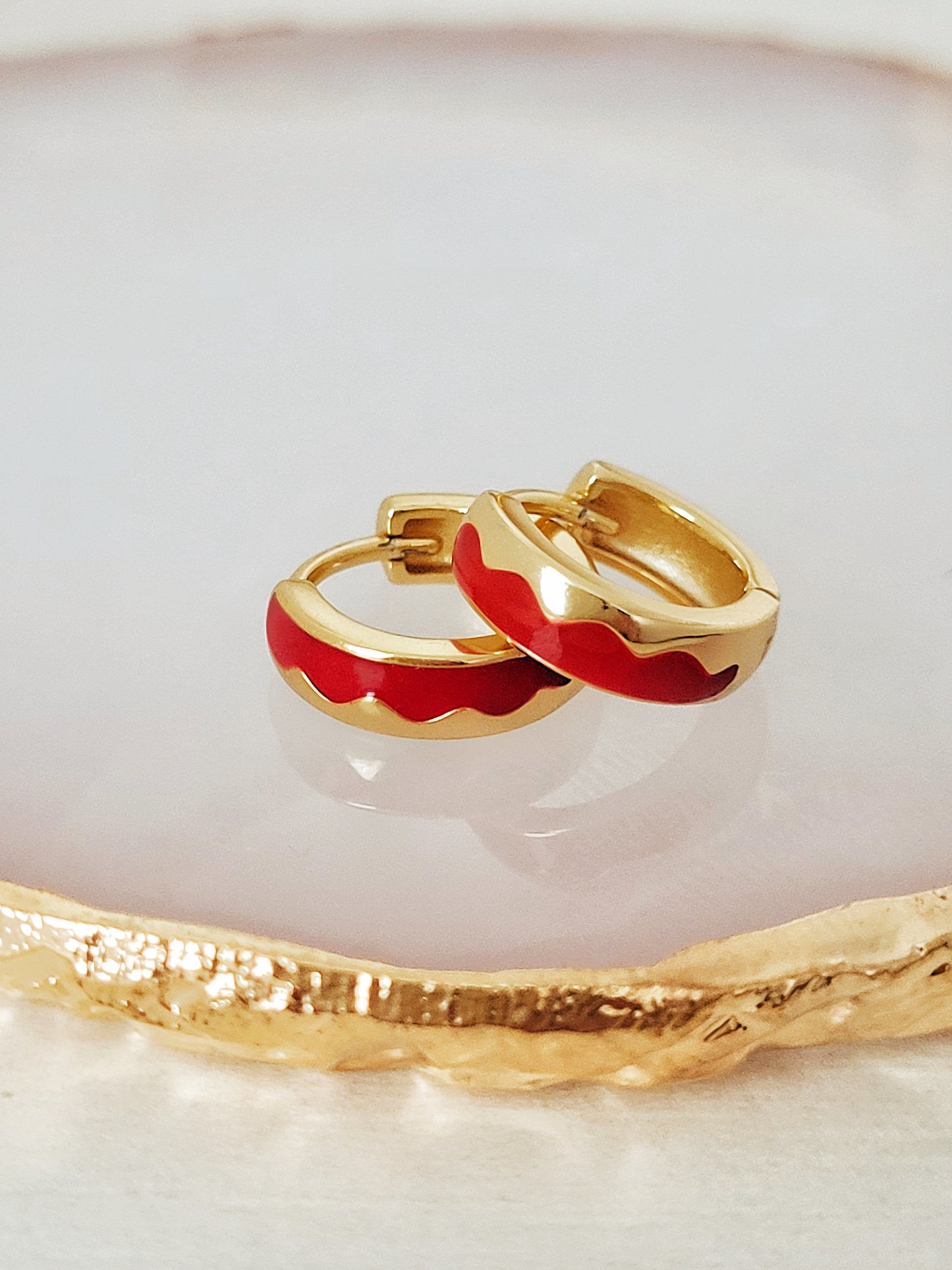 Stunning gold-plated huggie hoops with wavy pattern featuring rich red enamel, a luxurious accessory for any sophisticated ensemble.