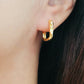 A woman elegantly wears a gold ear cuff alongside hammered hoop earrings, emphasizing her chic and modern style.