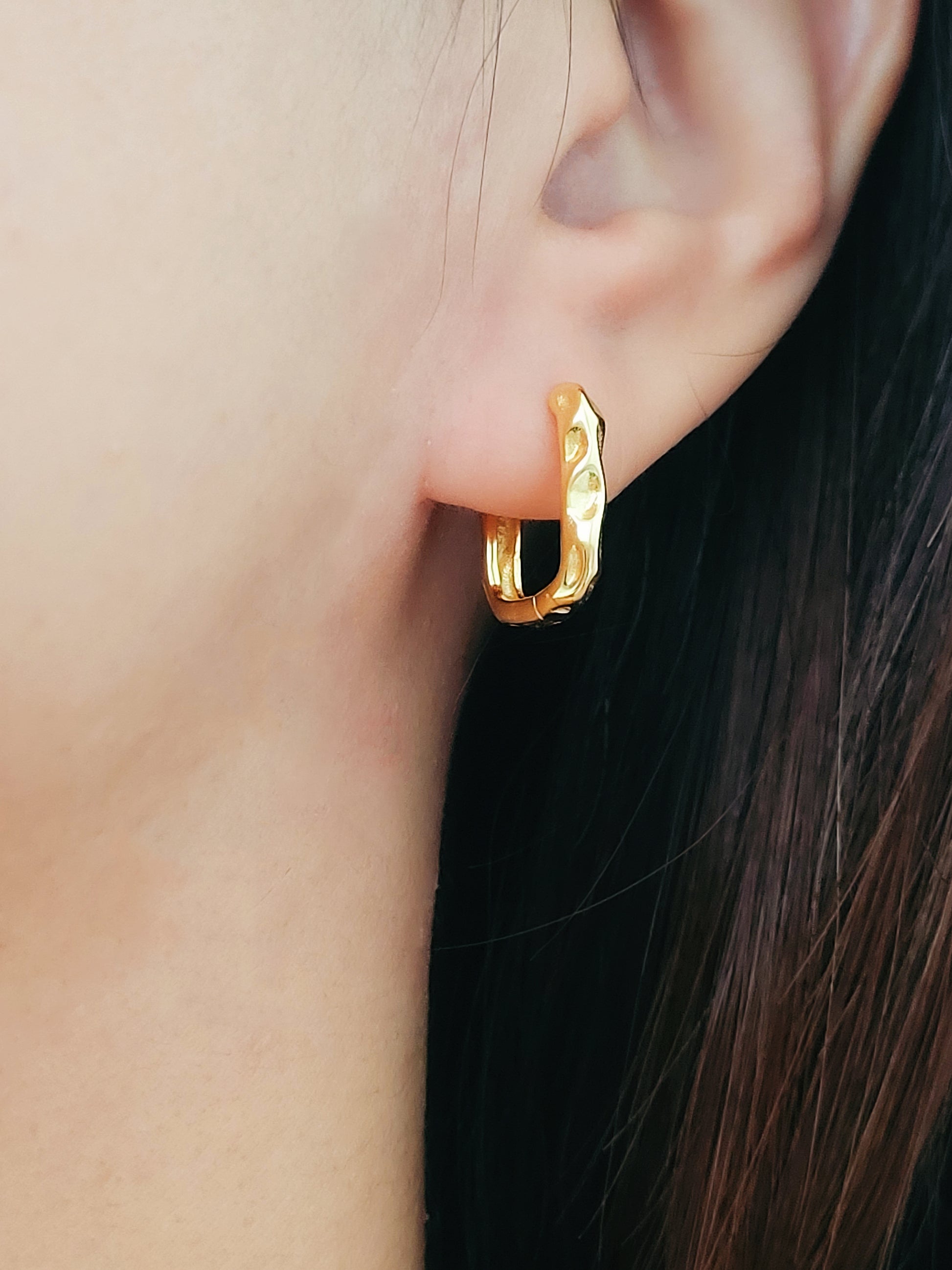 A woman elegantly wears a gold ear cuff alongside hammered hoop earrings, emphasizing her chic and modern style.