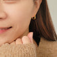 A stylish woman in a brown sweater elegantly wears hammered gold hoop earrings, embodying grace and refined taste.