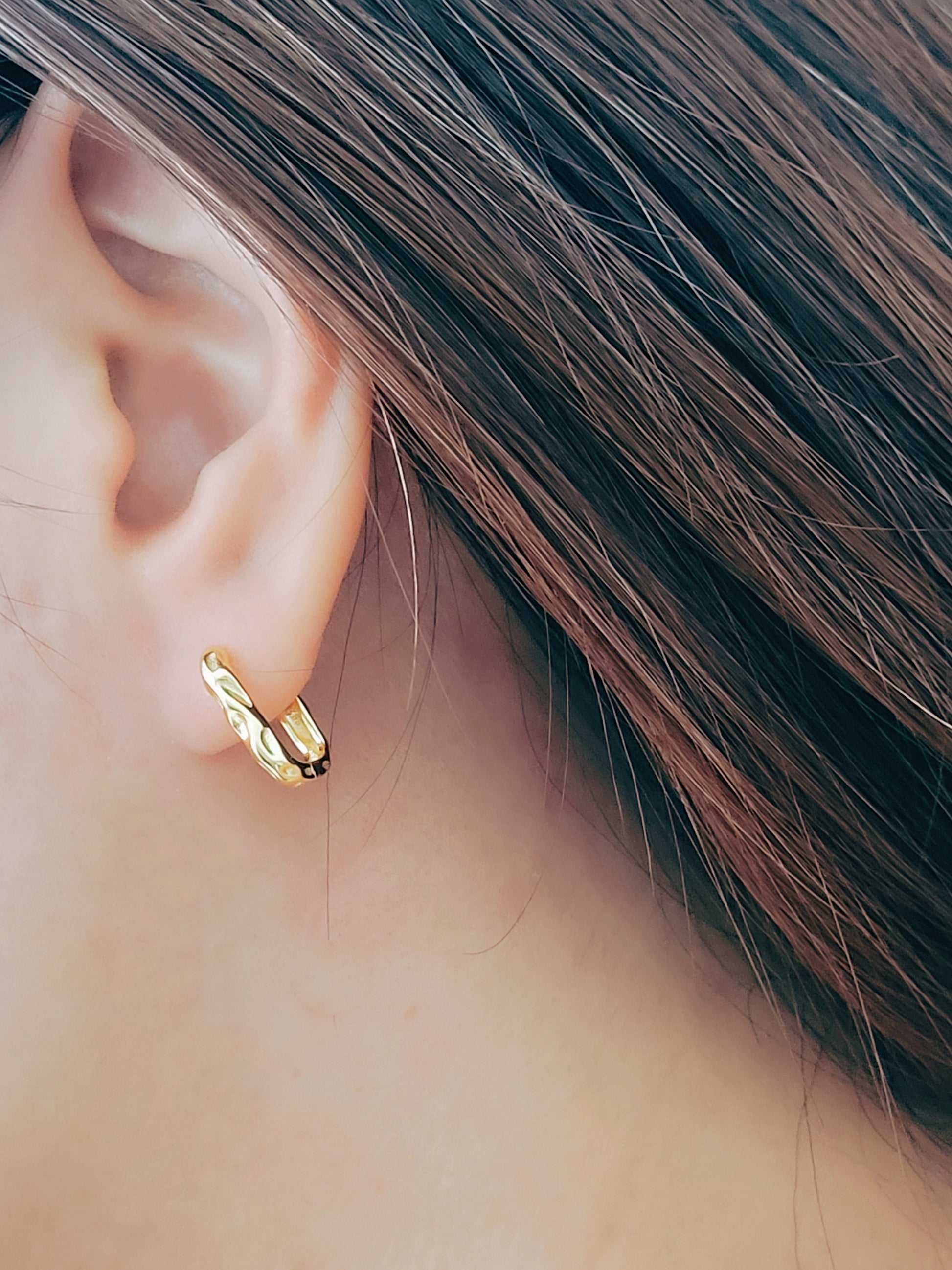 A woman showcases a stylish gold ear cuff paired with hammered hoop earrings, highlighting her unique fashion sense