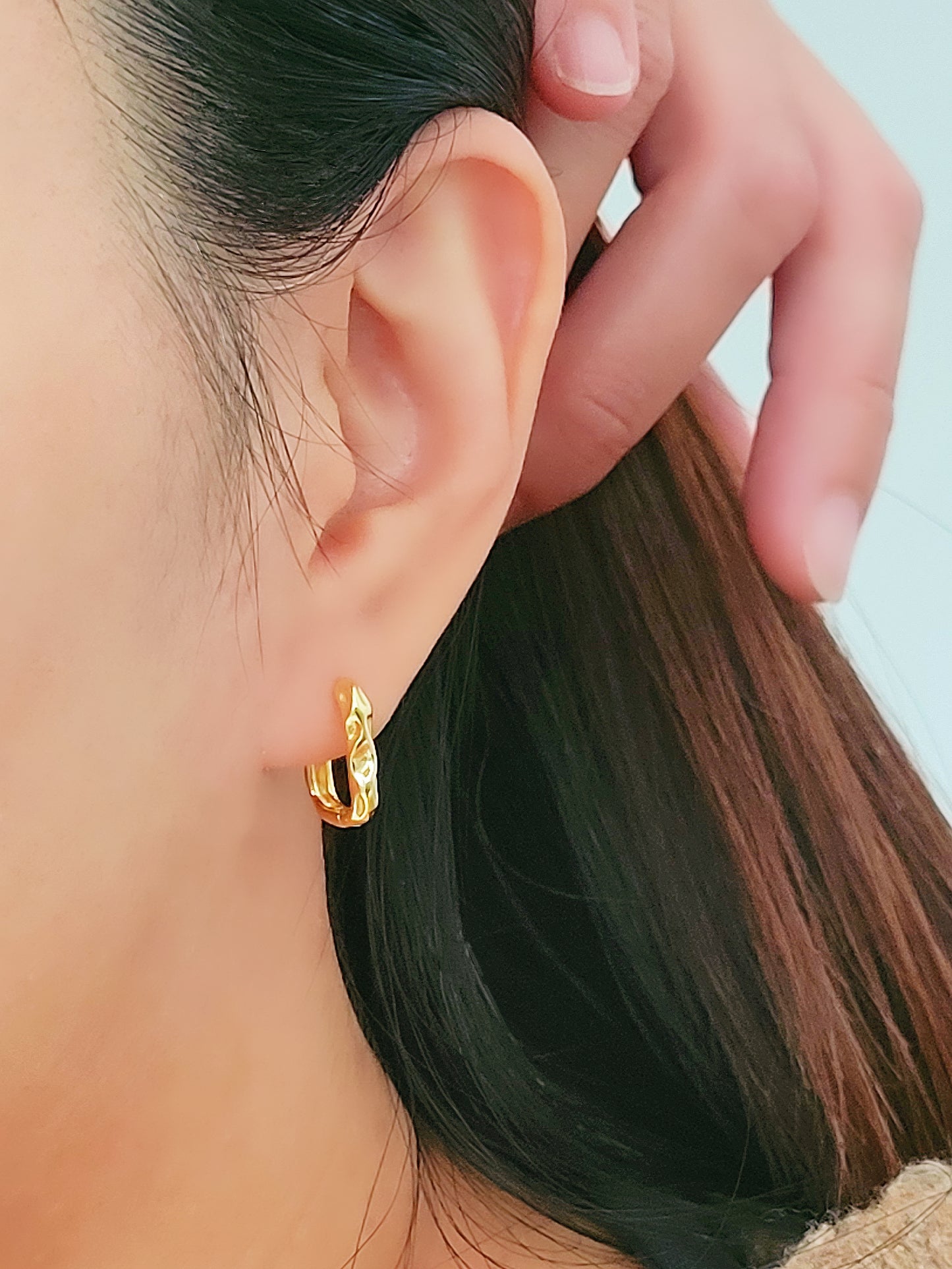 A woman showcases her elegance with hammered gold hoop earrings, exuding timeless sophistication.