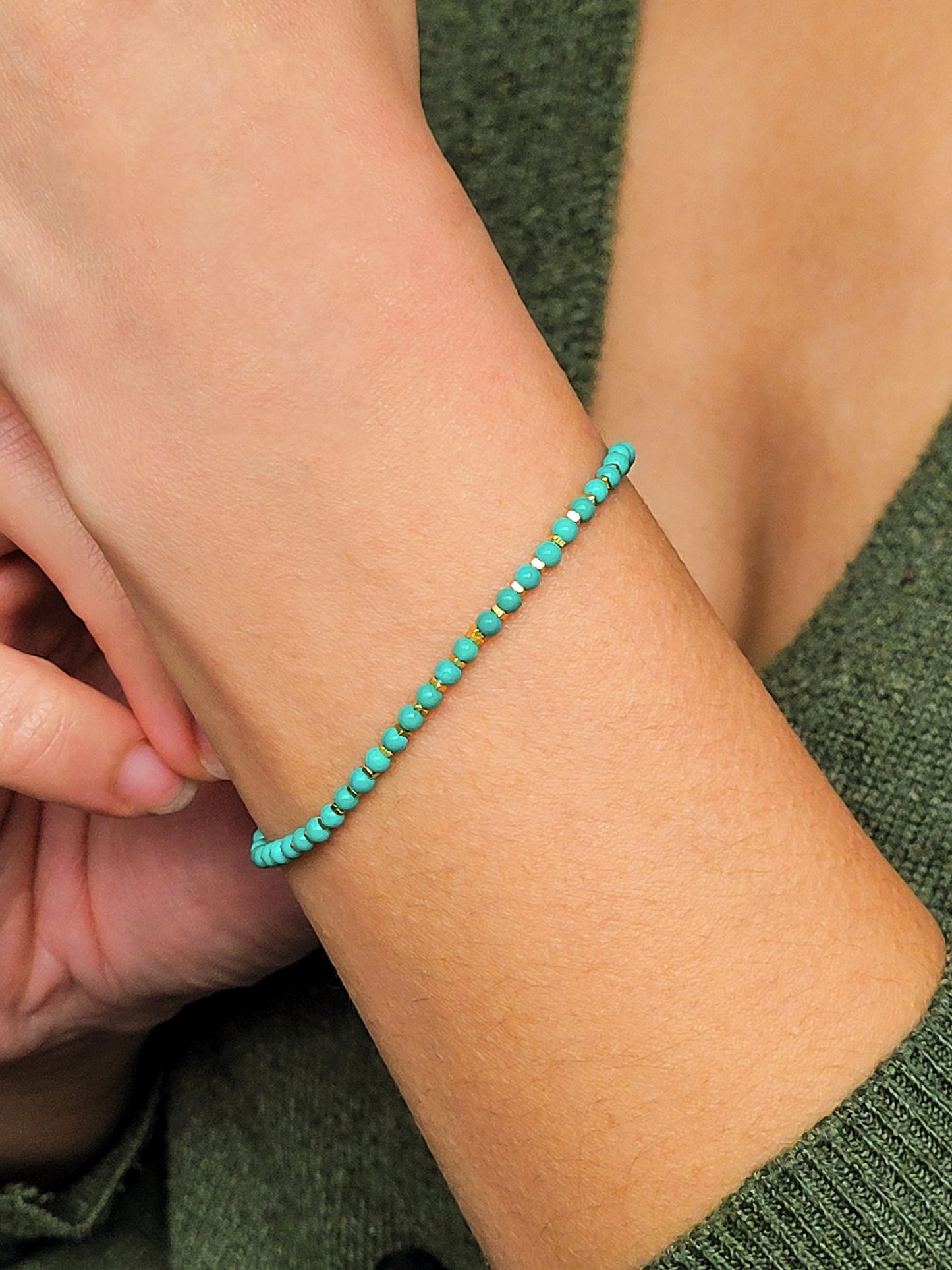 Close up of a woman's wrist wearing a Gold Turquoise beaded bracelet. Crafted in high quality natural turquoise gemstone intersecting with gold vermeil beads.