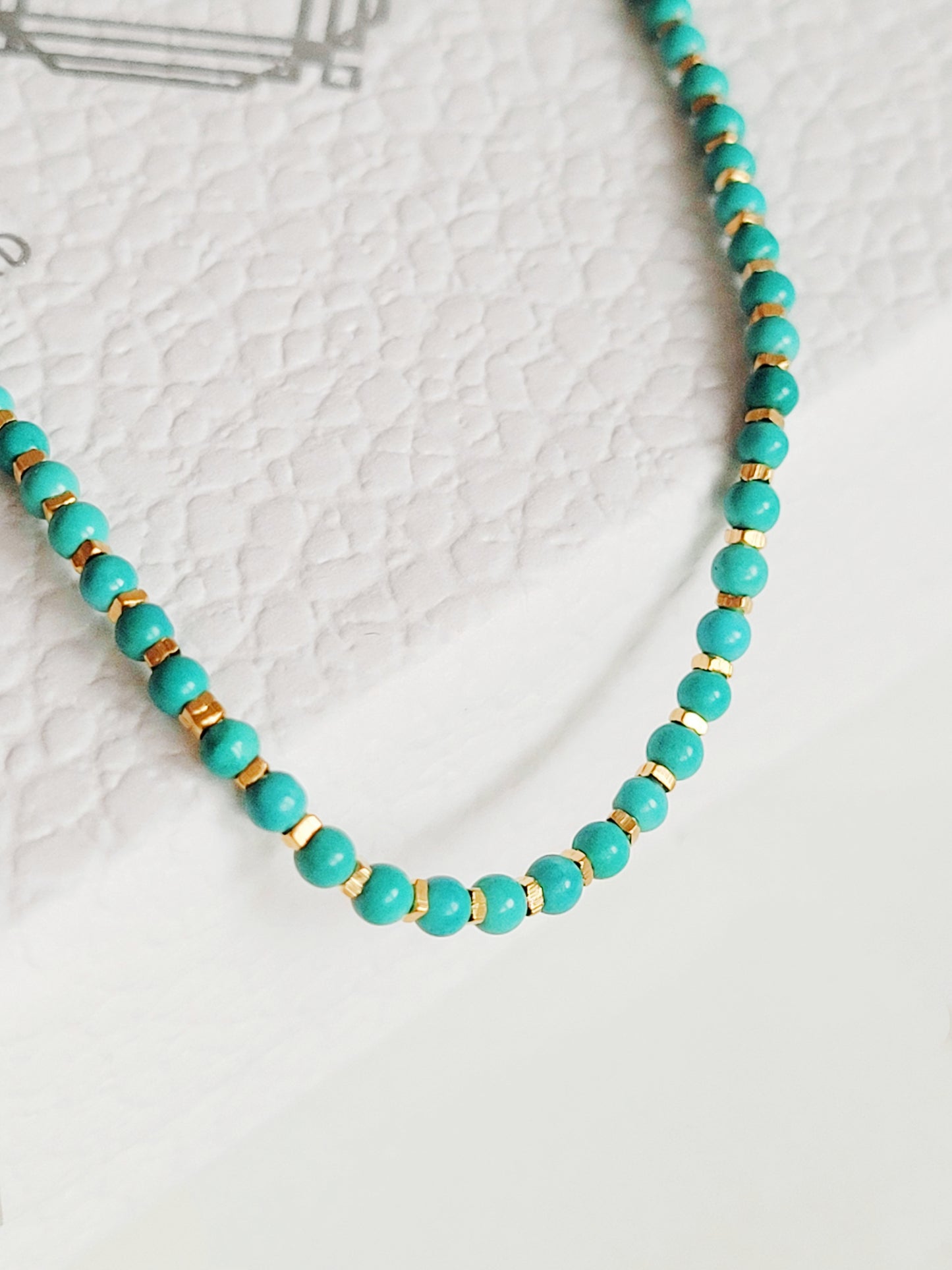 Close up of a Gold Turquoise beaded bracelet displayed on a white surface. Crafted in natural turquoise gemstone intersecting with gold vermeil beads.