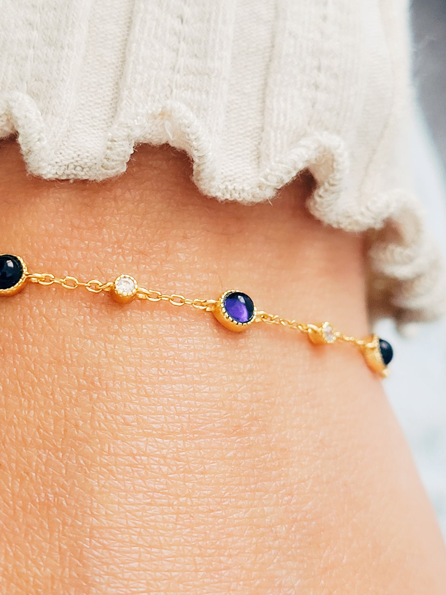 A woman elegantly showcases a sapphire station bracelet adorned with shimmering natural sapphire gemstones and radiant gold plated chain.