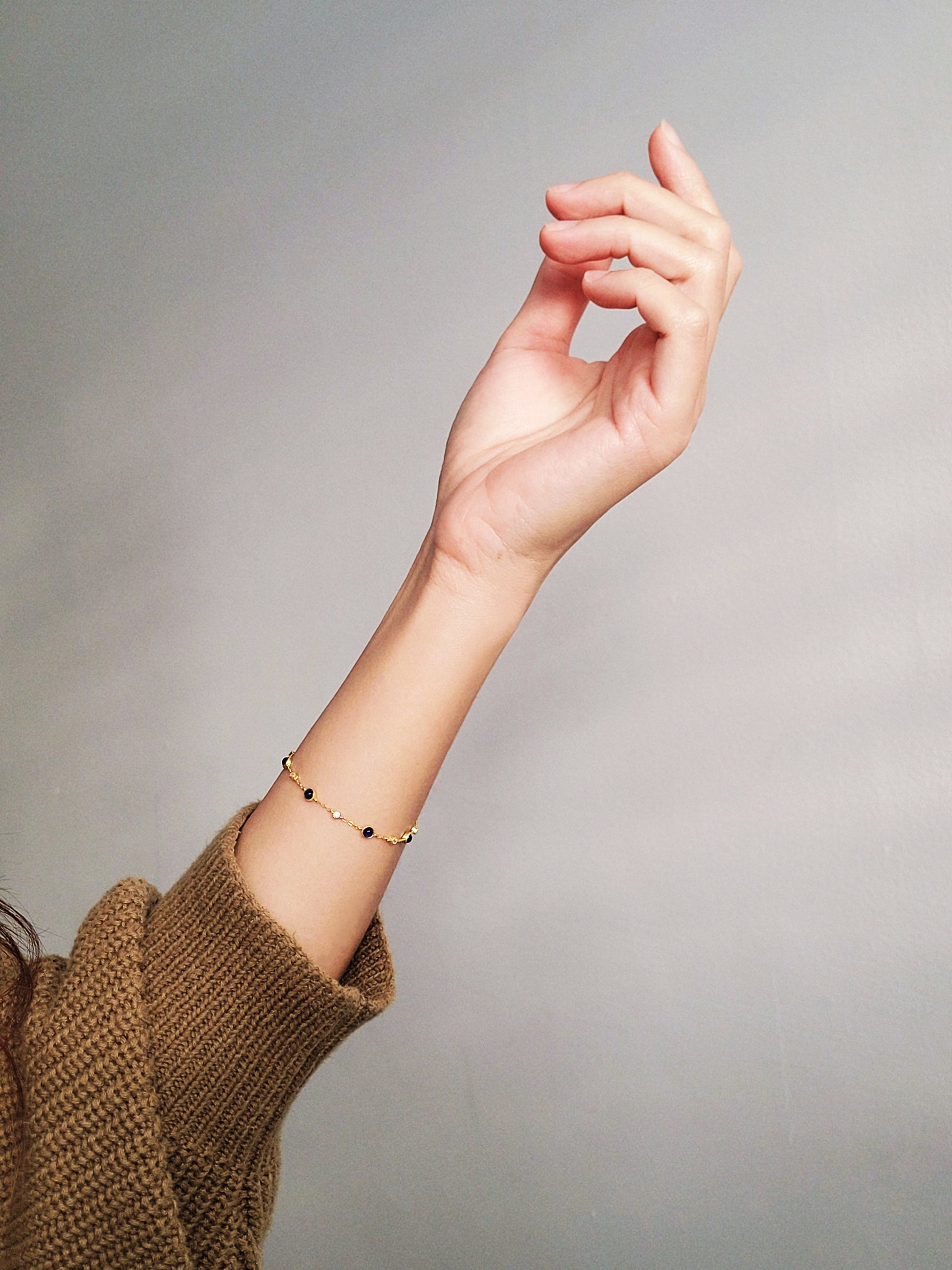 A woman's hand displays a luxurious gold bracelet featuring exquisite genuine sapphire stones, and shinny zircons stones embodying elegance and sophistication.