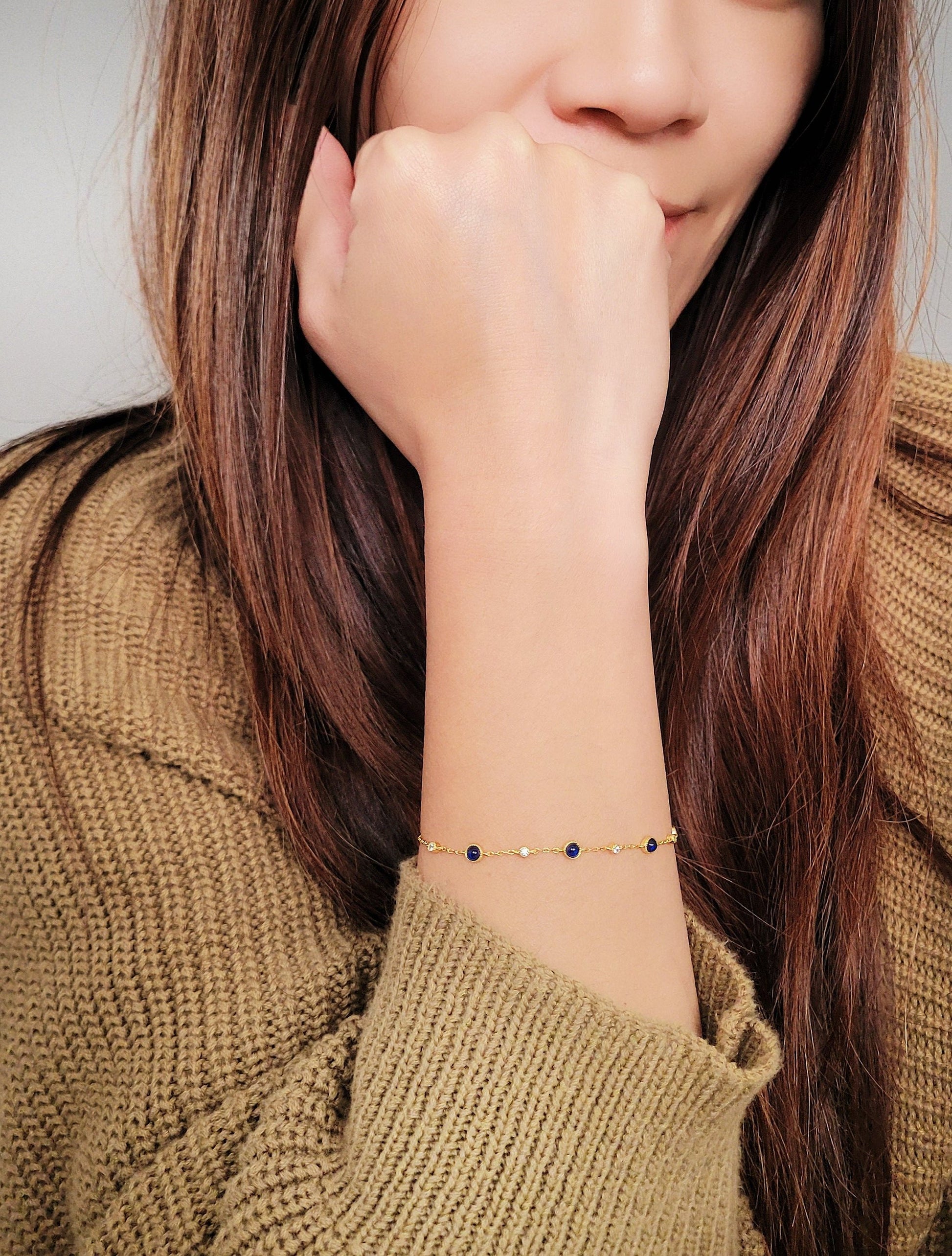 A woman elegantly showcases a real sapphire station bracelet adorned with a luxurious gold chain and small cubic zirconia.