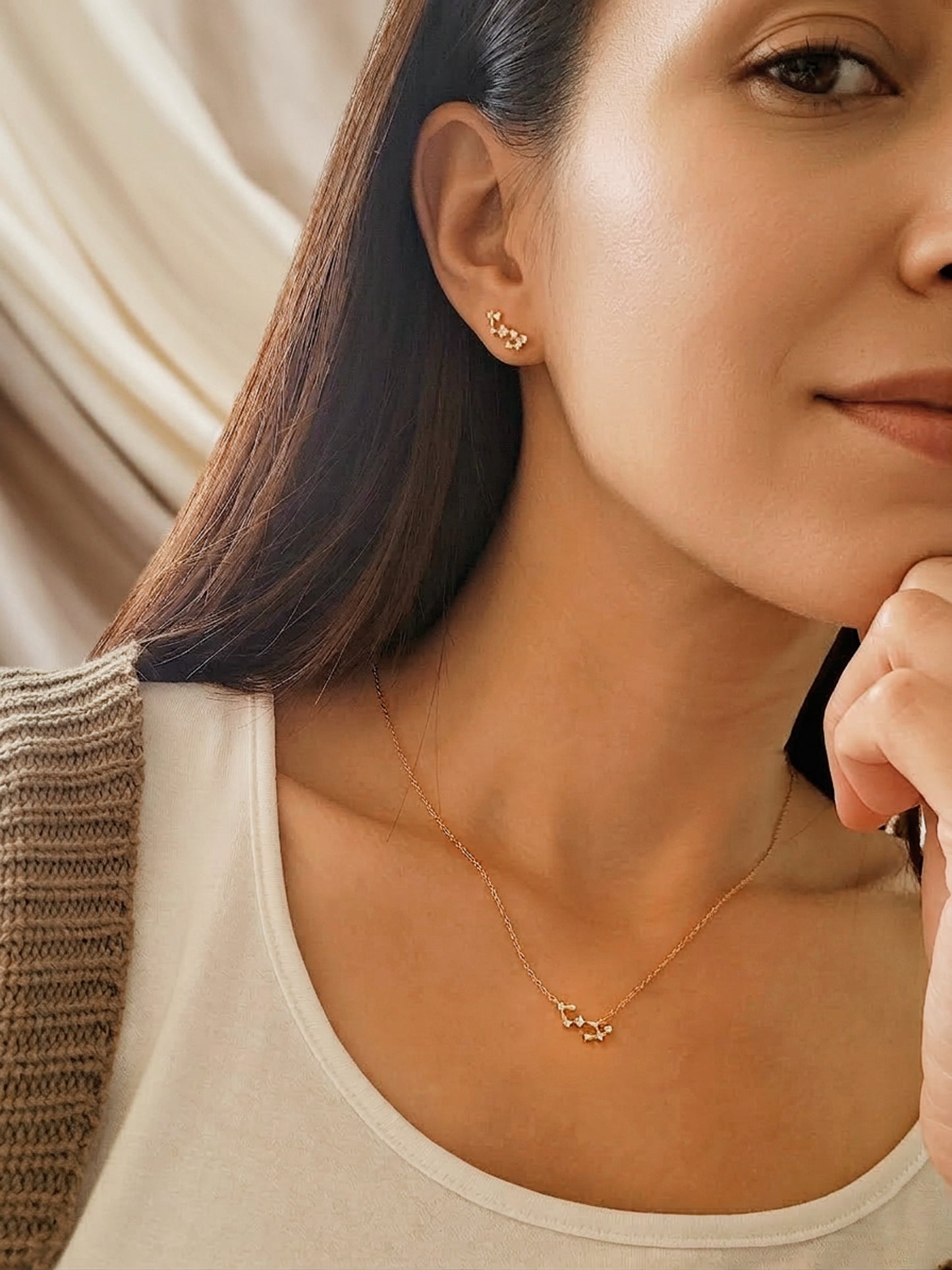 A woman wearing gold scorpio constellation star sign earring and a Scorpio necklace with a neutral background