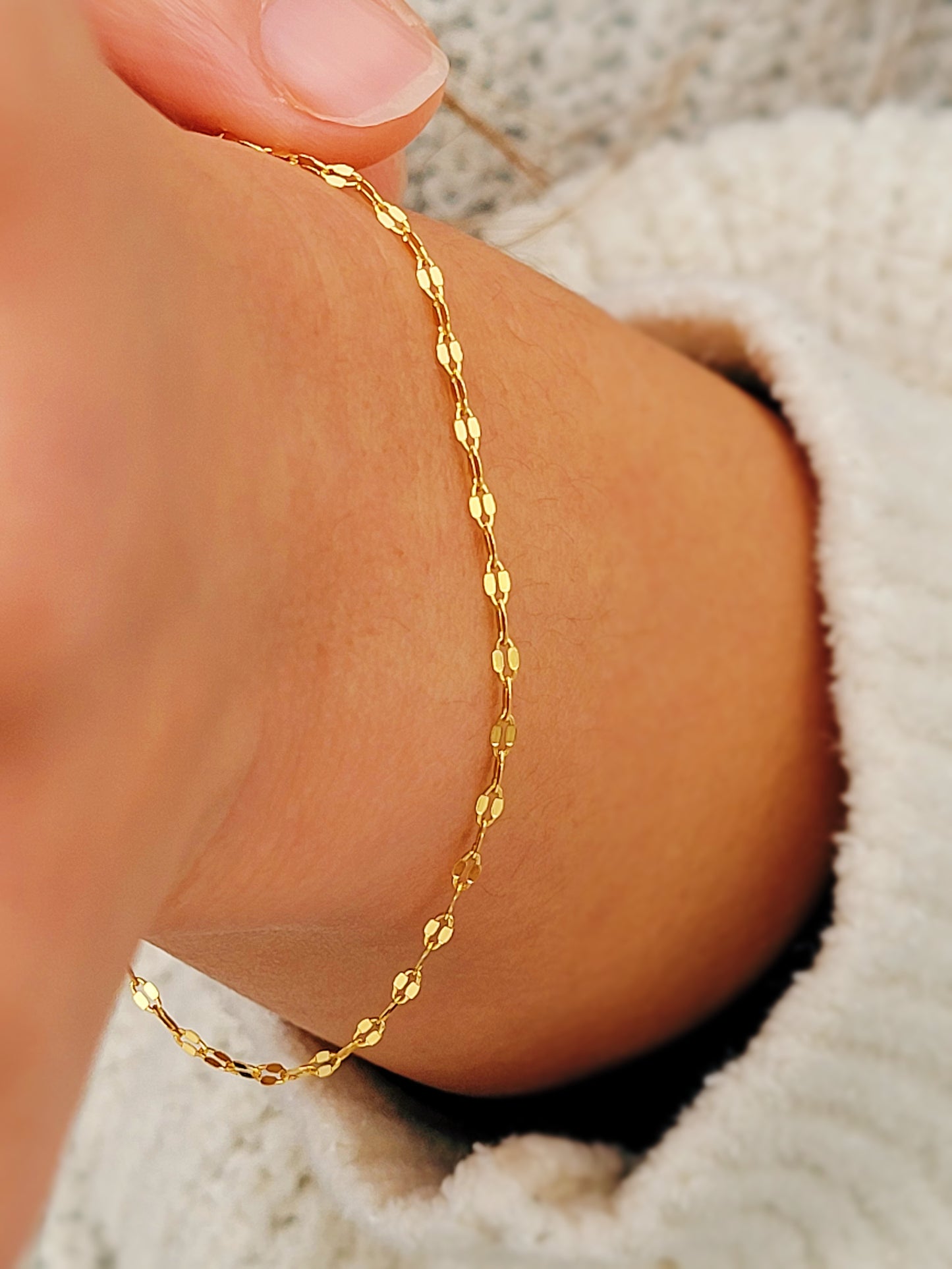 Woman wearing a delicate, gold vermeil skinny chain bracelet on her wrist, adding a subtle shimmer to her cozy. The bracelet&#39;s light-reflecting quality highlights its minimalist design, creating an elegant and understated style.