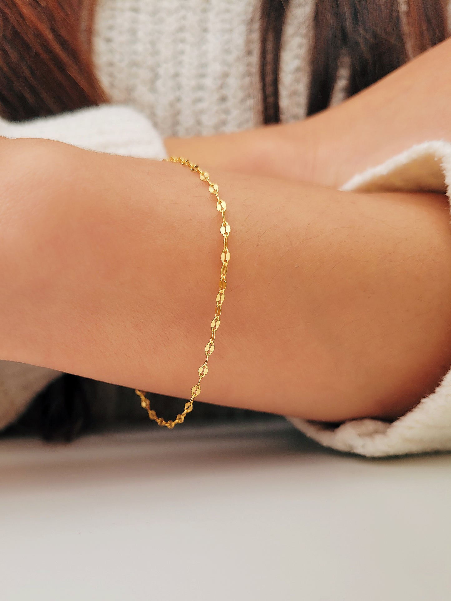 Woman wearing a delicate, gold vermeil skinny chain bracelet on her wrist, adding a subtle shimmer to her cozy. The bracelet&#39;s light-reflecting quality highlights its minimalist design, creating an elegant and understated style.