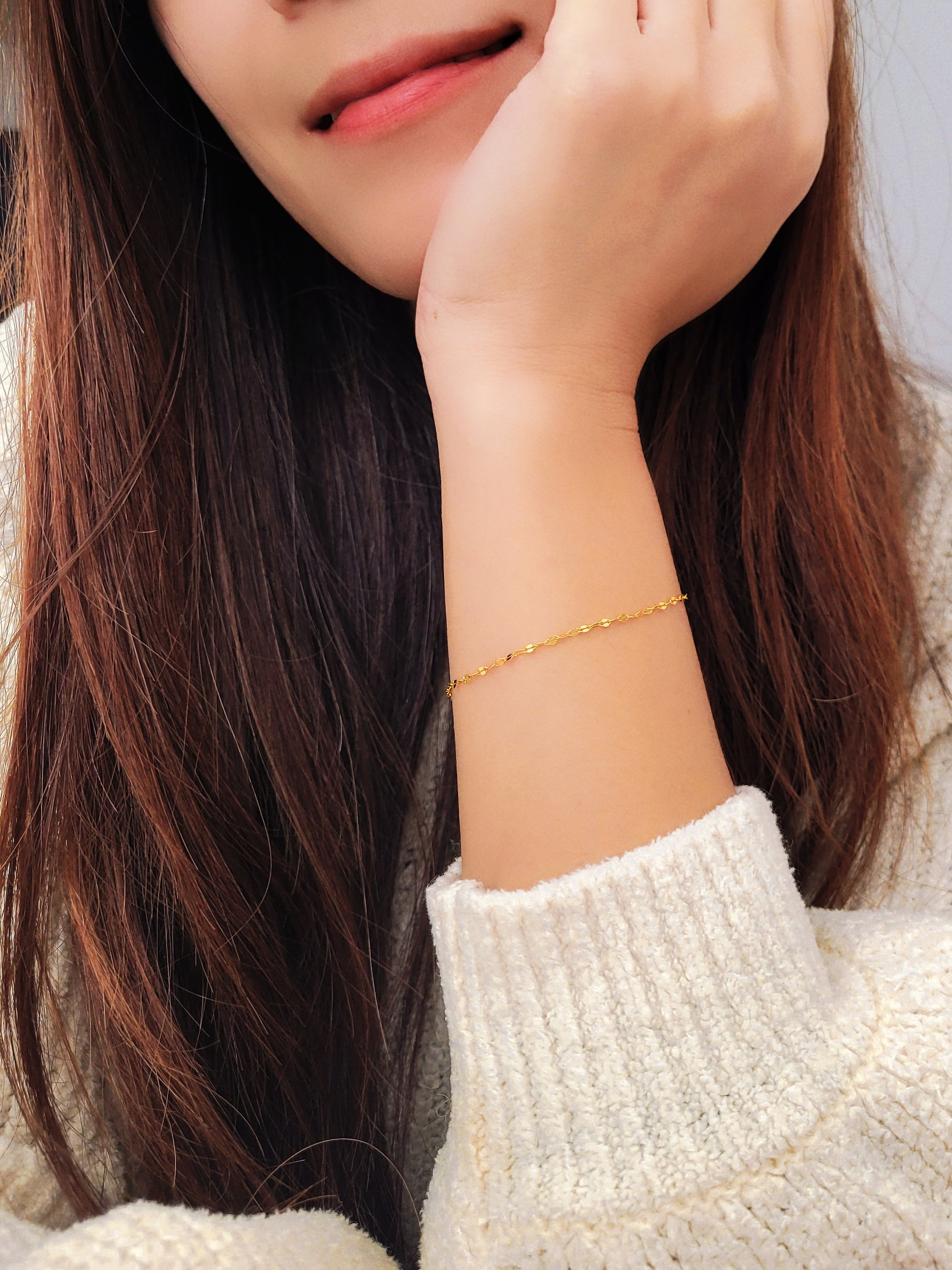 Woman wearing a delicate, gold vermeil skinny chain bracelet on her wrist, adding a subtle shimmer to her cozy, casual look with a soft white sweater. The bracelet's light-reflecting quality highlights its minimalist design, creating an elegant and understated style.