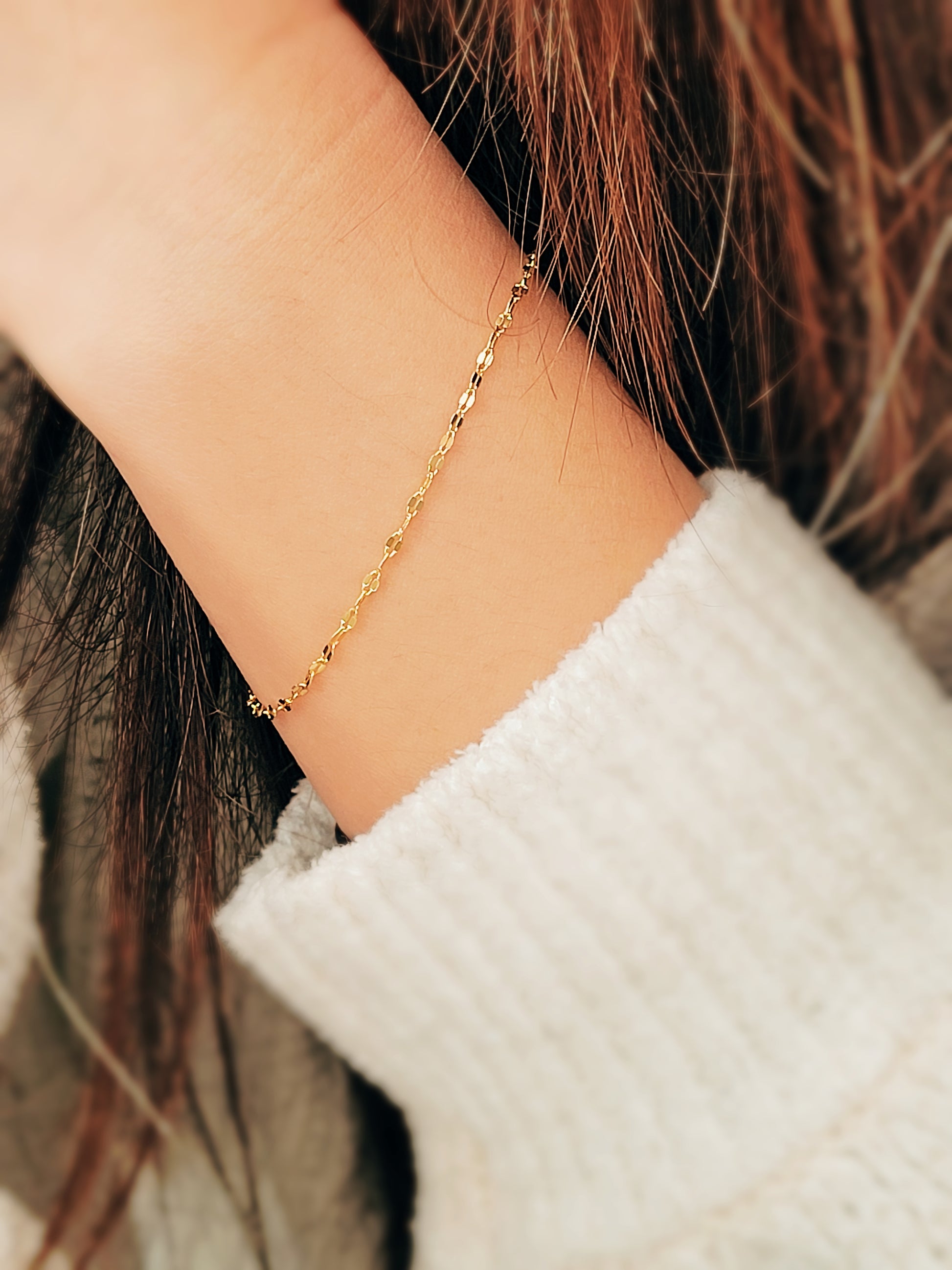 Woman wearing a delicate, gold vermeil skinny chain bracelet on her wrist, adding a subtle shimmer to her cozy. The bracelet's light-reflecting quality highlights its minimalist design, creating an elegant and understated style.