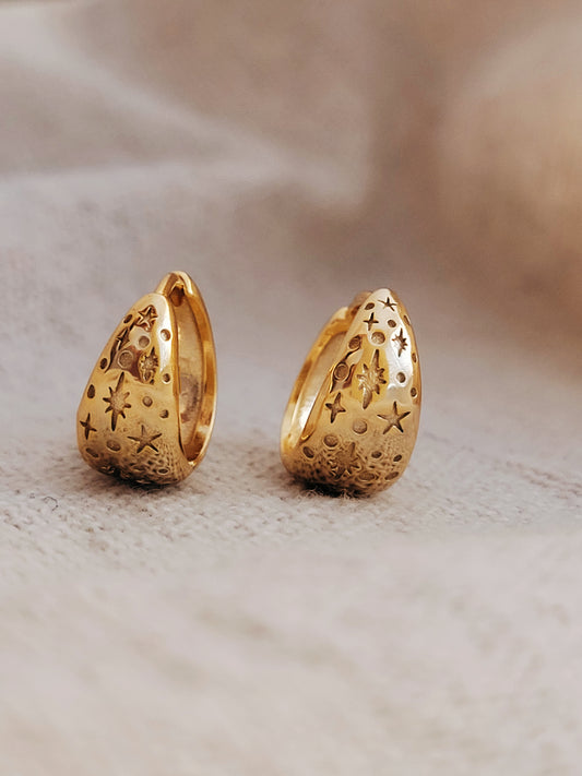 Pair of gold star hoop earrings with intricate starry designs on a beige background